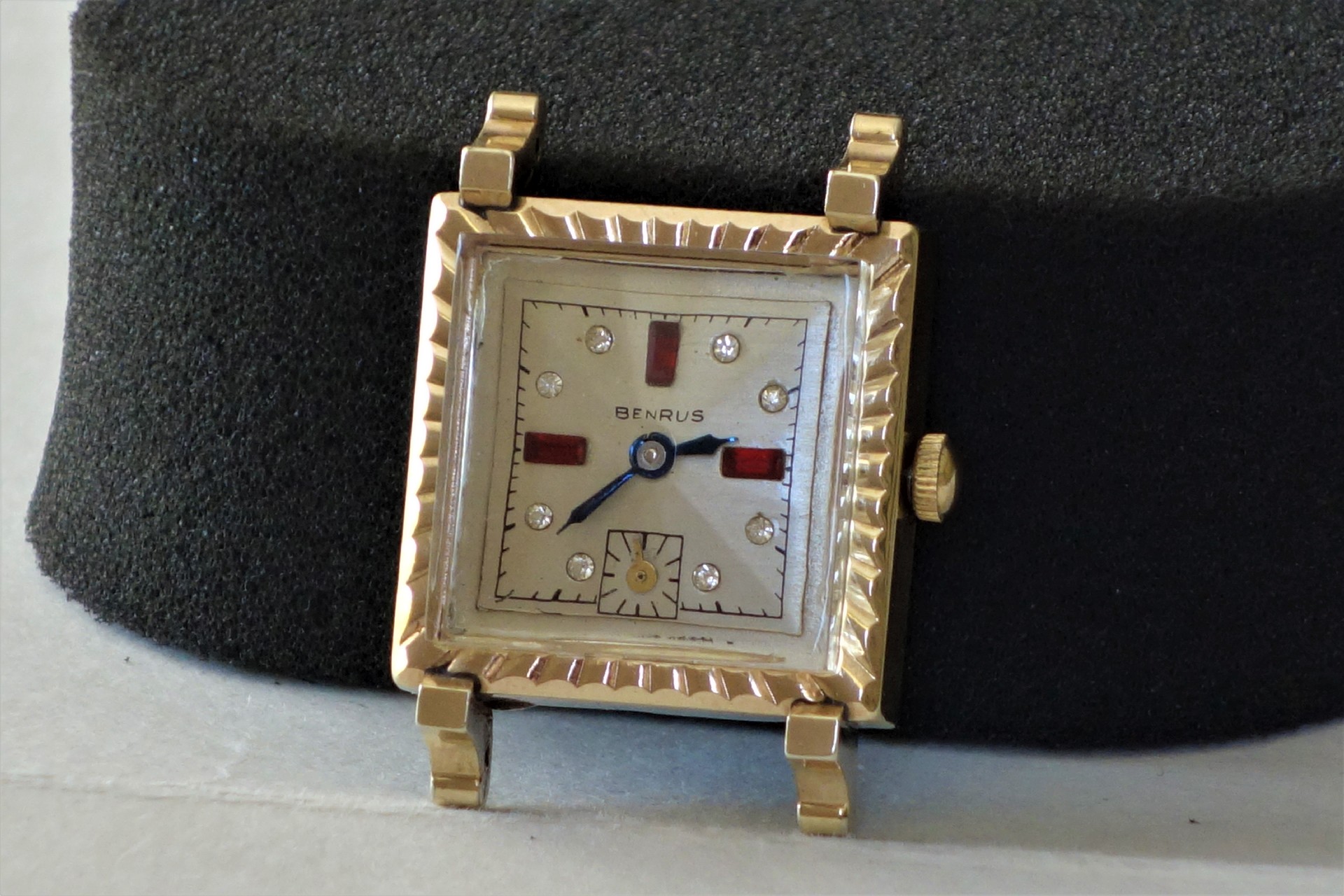 Rechteckige Armbanduhr mit hellem Zifferblatt, roten und silbernen Indizes sowie Metallgehäuse.