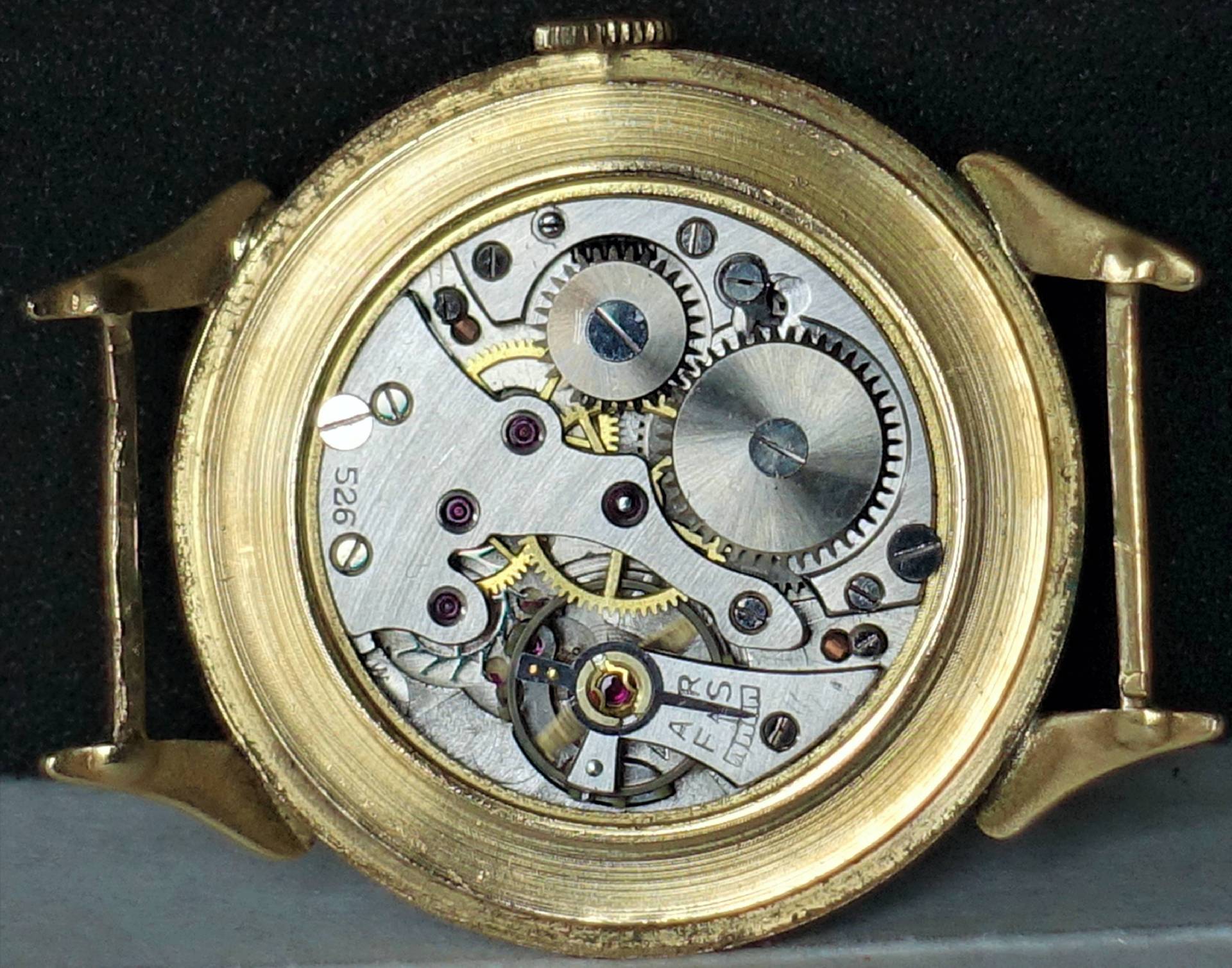 Mechanisches Uhrwerk in einem goldfarbenen Uhrengehäuse, sichtbare Zahnräder und Schrauben.