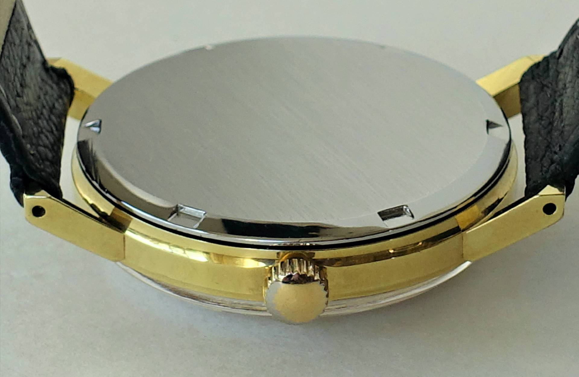 Rückseite eines goldfarbenen Uhrgehäuses mit silberfarbenem Boden und schwarzem Armband.