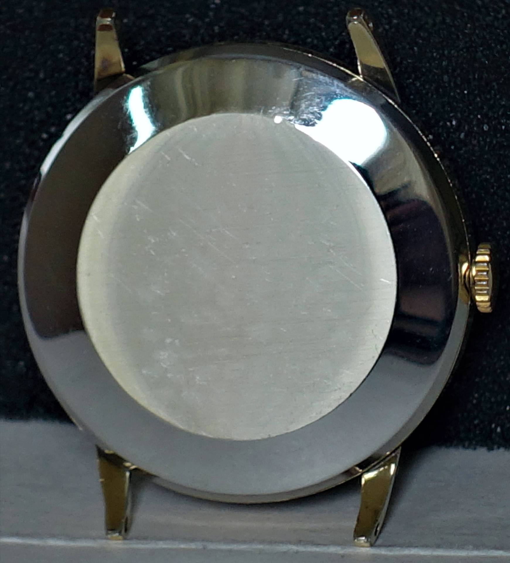 Rundes silberfarbenes Uhrgehäuse mit goldfarbener Krone und goldfarbenen Bandanstößen.