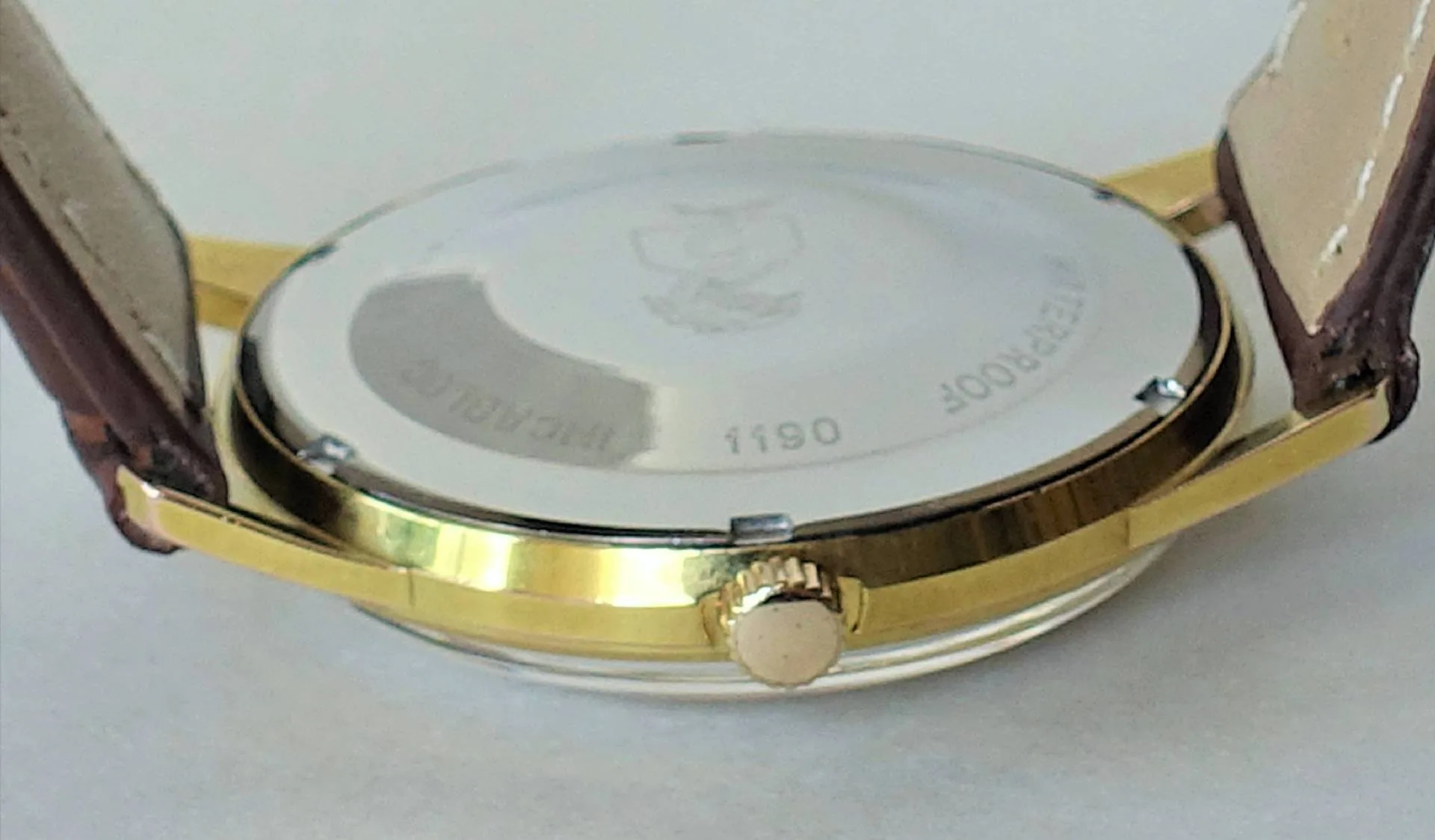 Die Rückseite einer Armbanduhr mit gelbfarbenem Gehäuse, silberfarbenem Boden und braunem Lederarmband ist zu sehen.