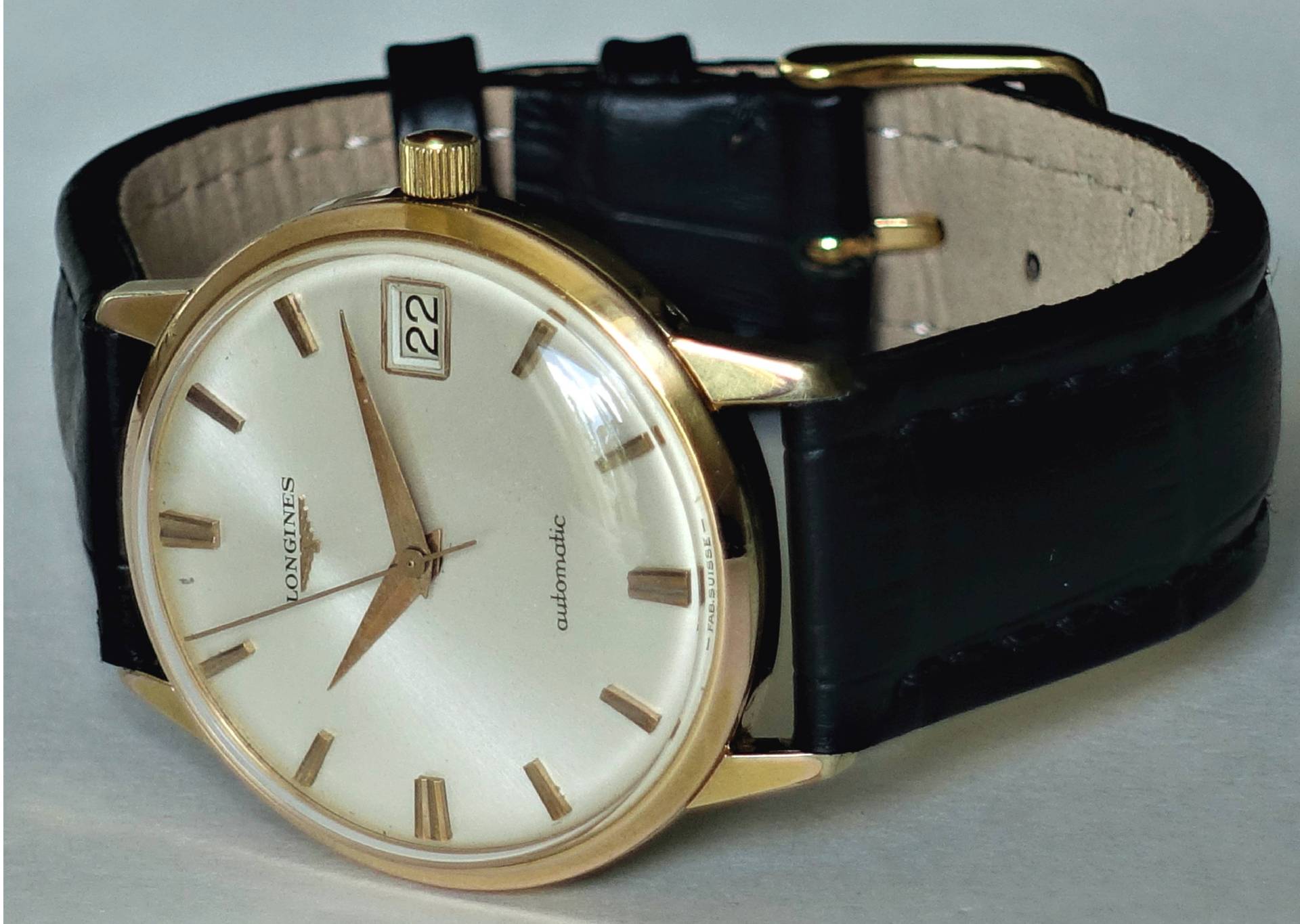 Klassische Armbanduhr mit goldfarbenem Gehäuse, hellem Zifferblatt und schwarzem Armband.