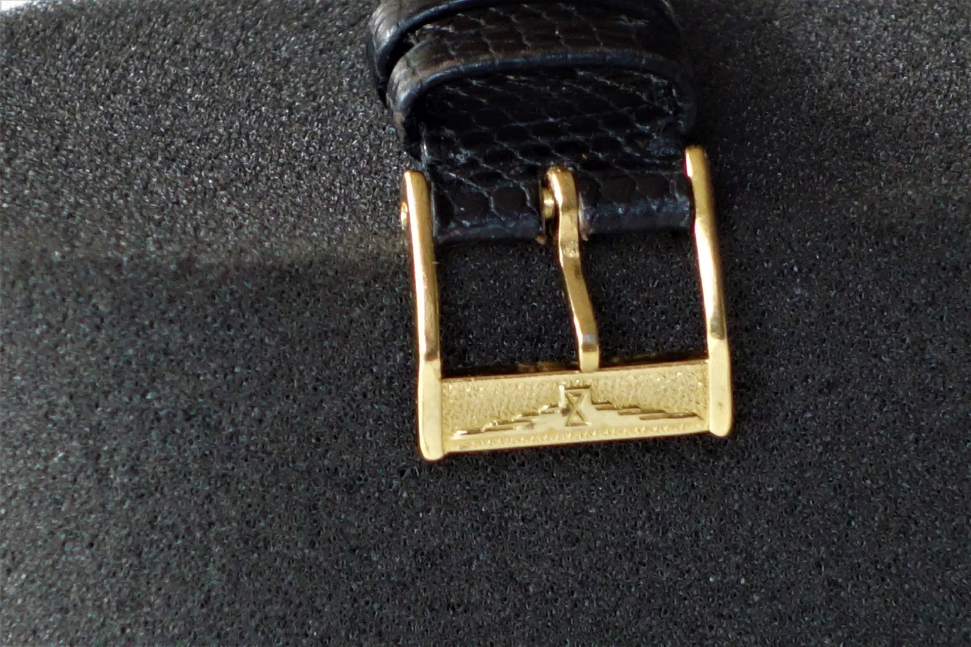 Goldfarbene Dornschließe an schwarzem Uhrenarmband aus Leder.