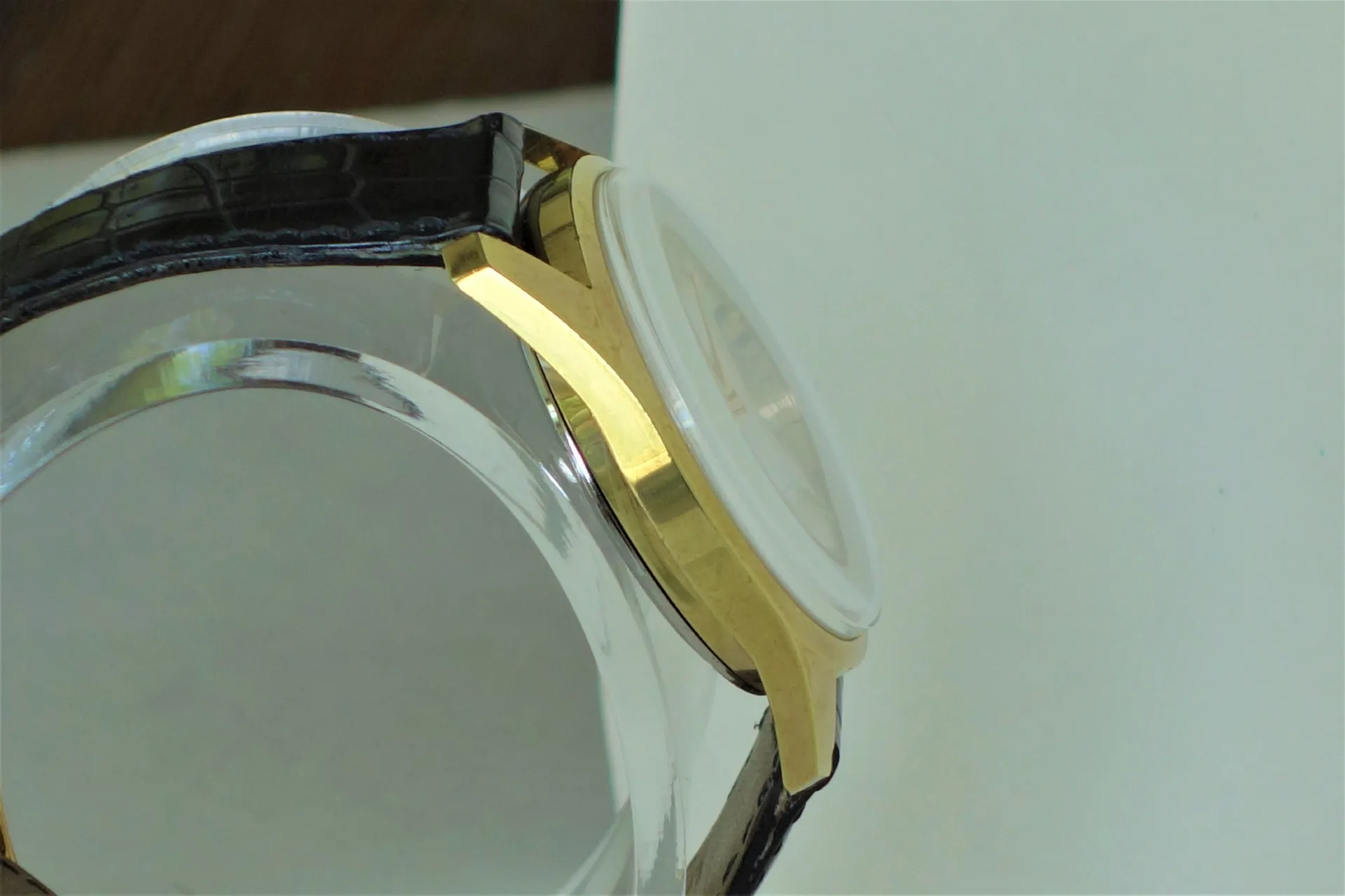Goldfarbenes Metallgehäuse für Armbanduhr mit schwarzem Lederarmband und gewölbtem Uhrglas.