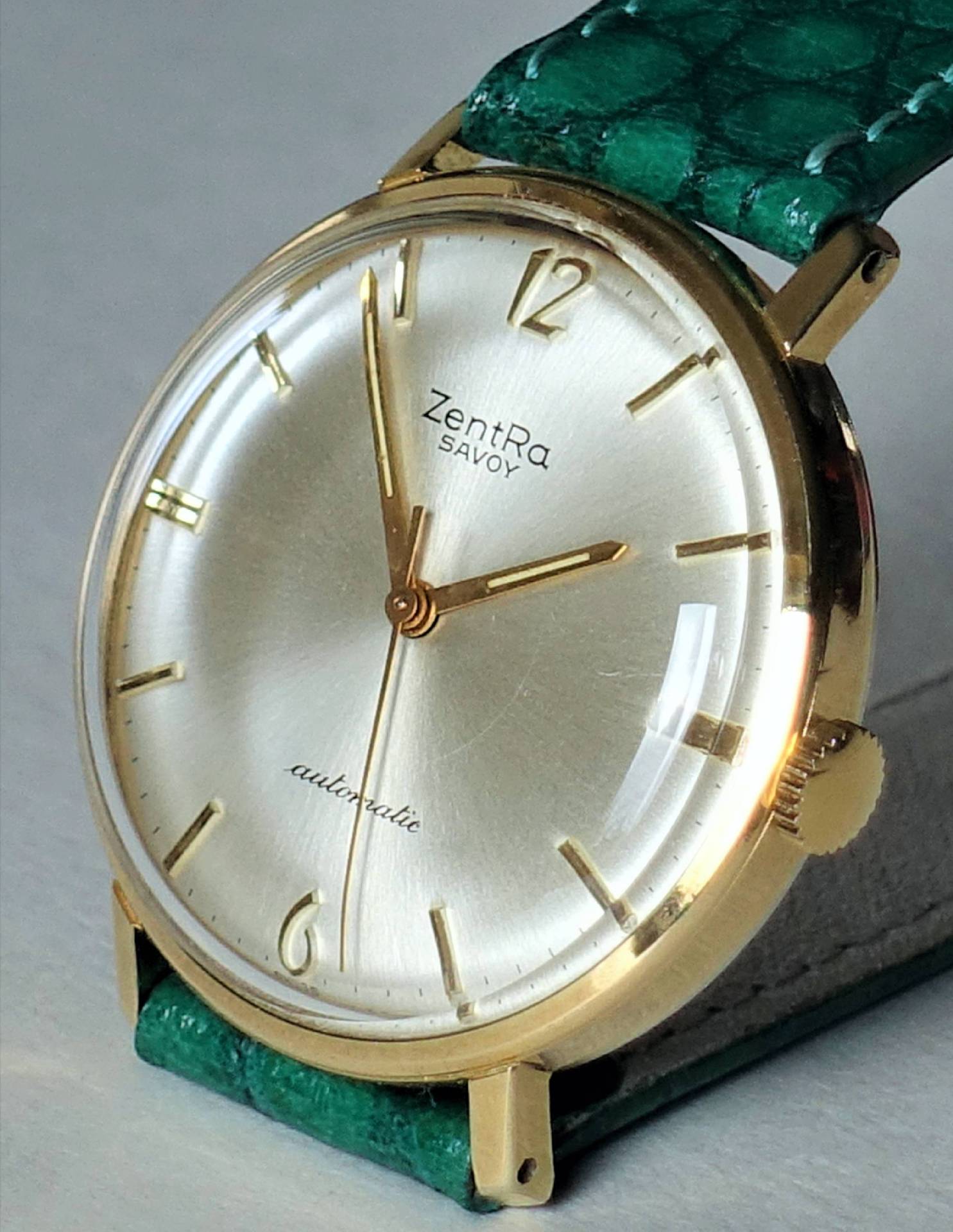 Goldfarbene Armbanduhr mit hellem Zifferblatt und grünem Armband.