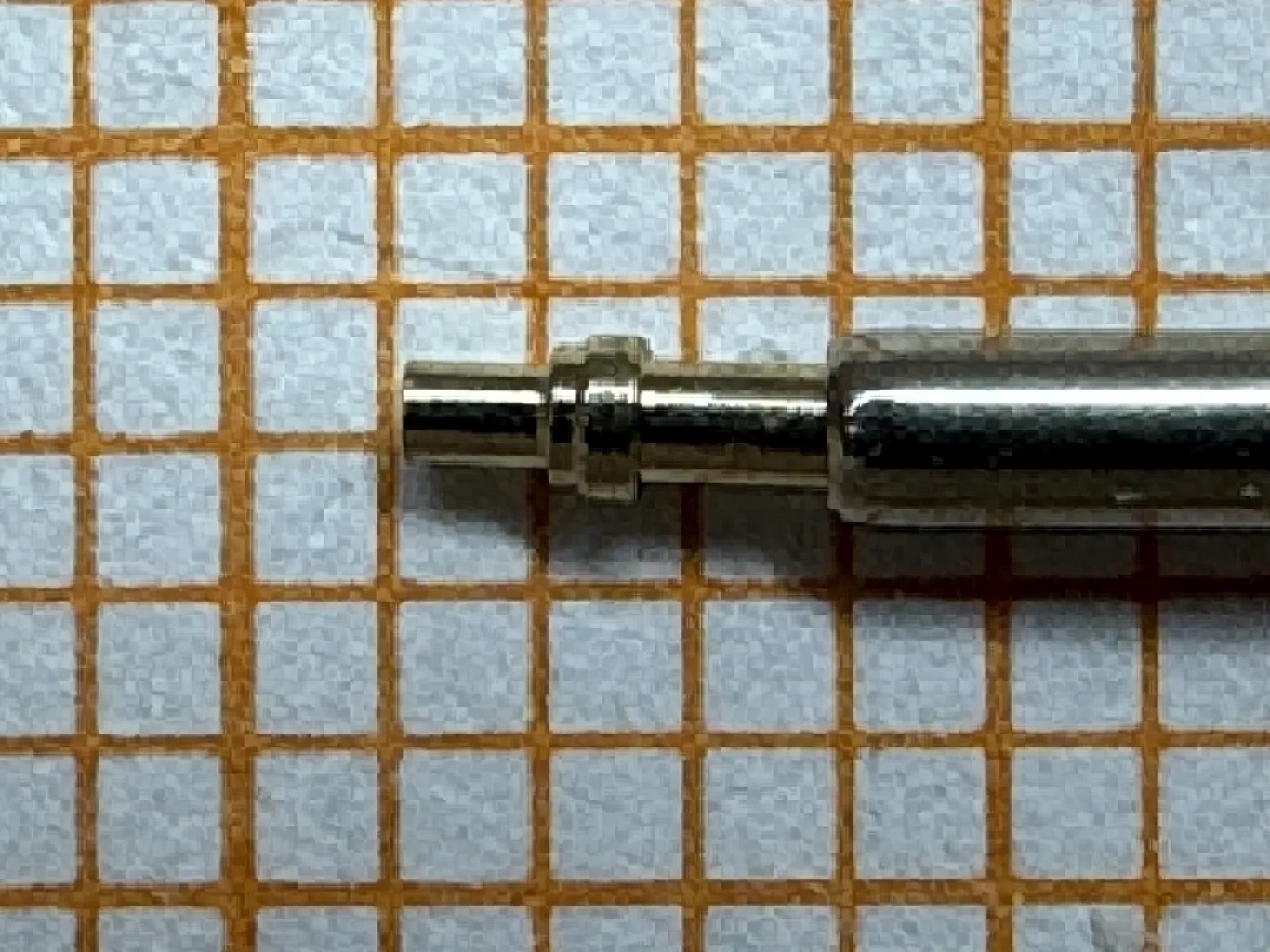Metallischer Federsteg für Uhrenarmbänder auf kariertem Hintergrund.