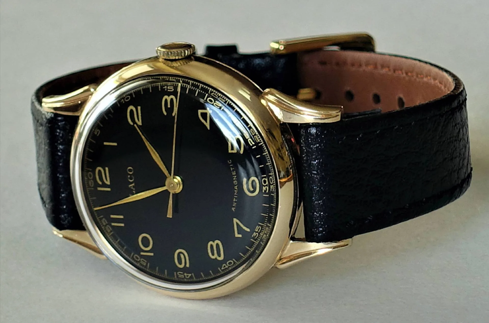 Schwarzes Zifferblatt, gelbfarbenes Gehäuse, schwarzes Lederband Eine Armbanduhr mit schwarzem Zifferblatt, gelbfarbenem Gehäuse und schwarzem Lederarmband liegt auf einer hellen Oberfläche.