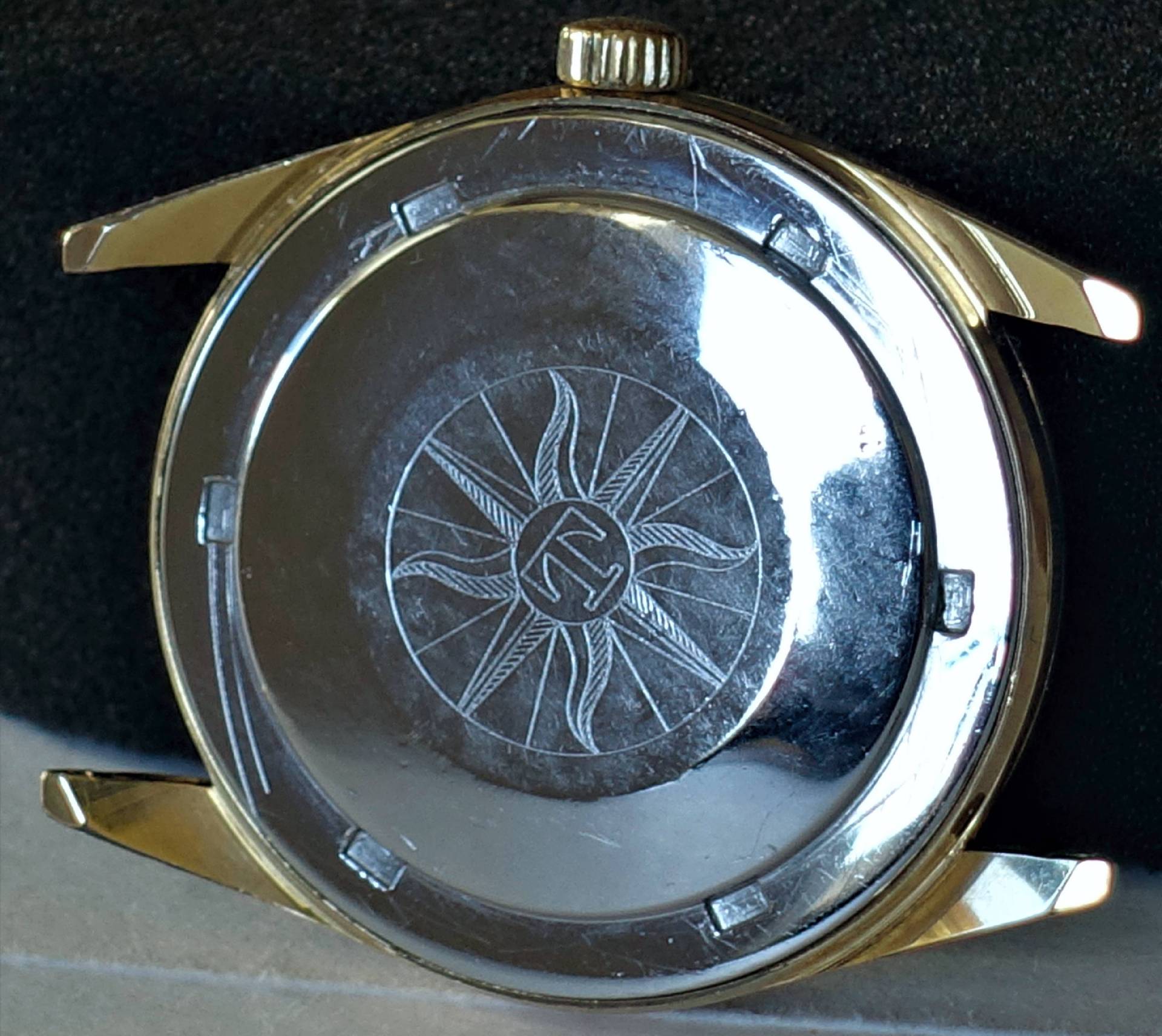 Rückseite eines goldfarbenen Uhrgehäuses mit graviertem Sonnensymbol.
