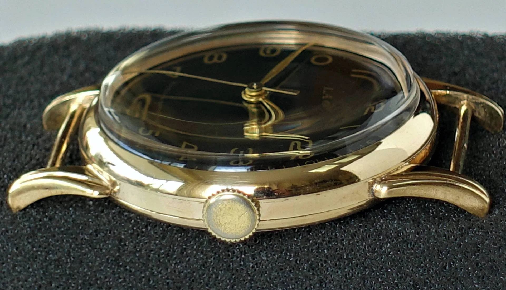 Schwarzes Zifferblatt, gelbes Gehäuse Eine Armbanduhr mit schwarzem Zifferblatt und gelbfarbenem Gehäuse liegt seitlich auf schwarzem Schaumstoff, das Glas ist stark gewölbt.