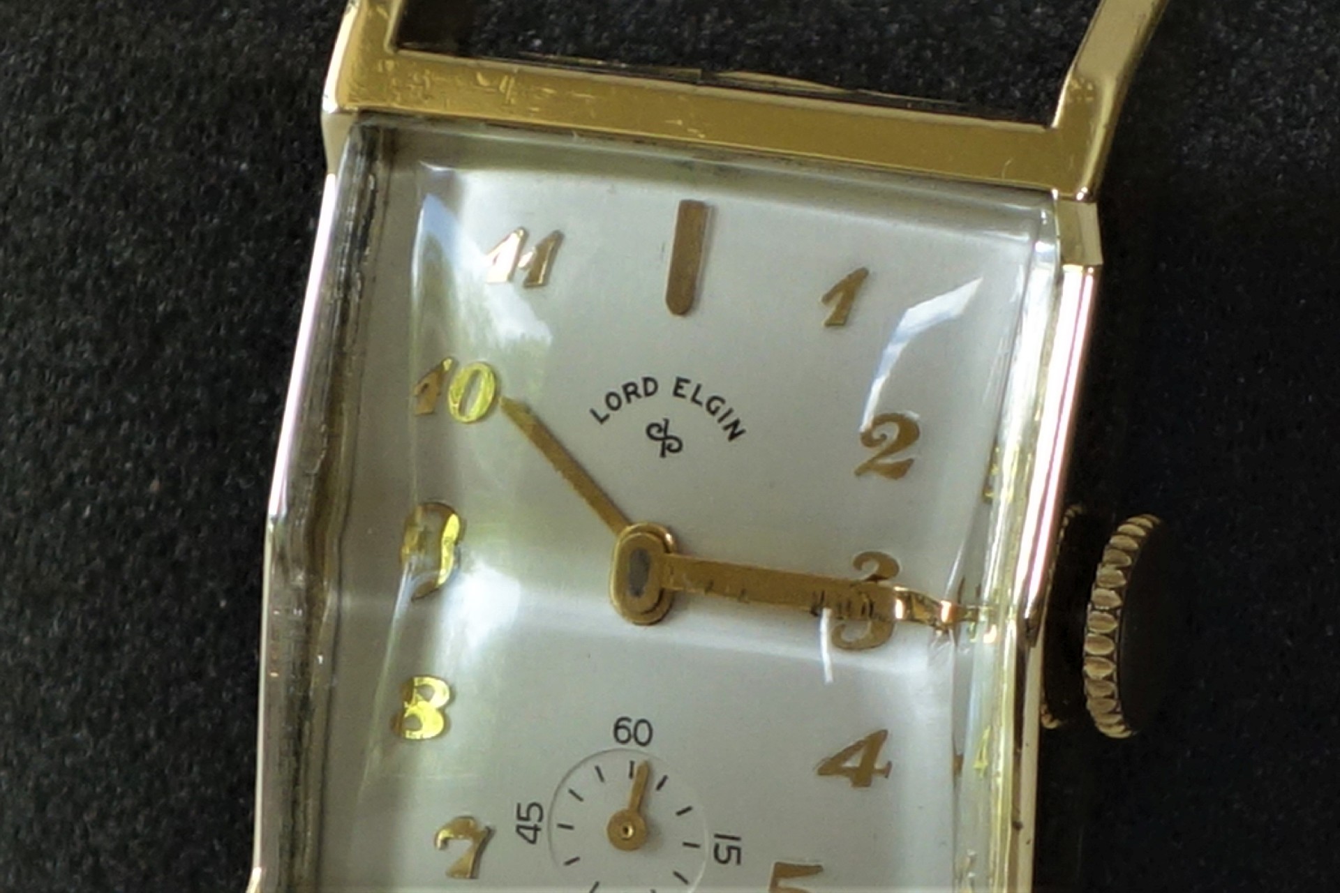 Rechteckige Armbanduhr mit goldfarbenem Gehäuse, weißen Zifferblatt und goldfarbenen Zahlen und Zeigern.