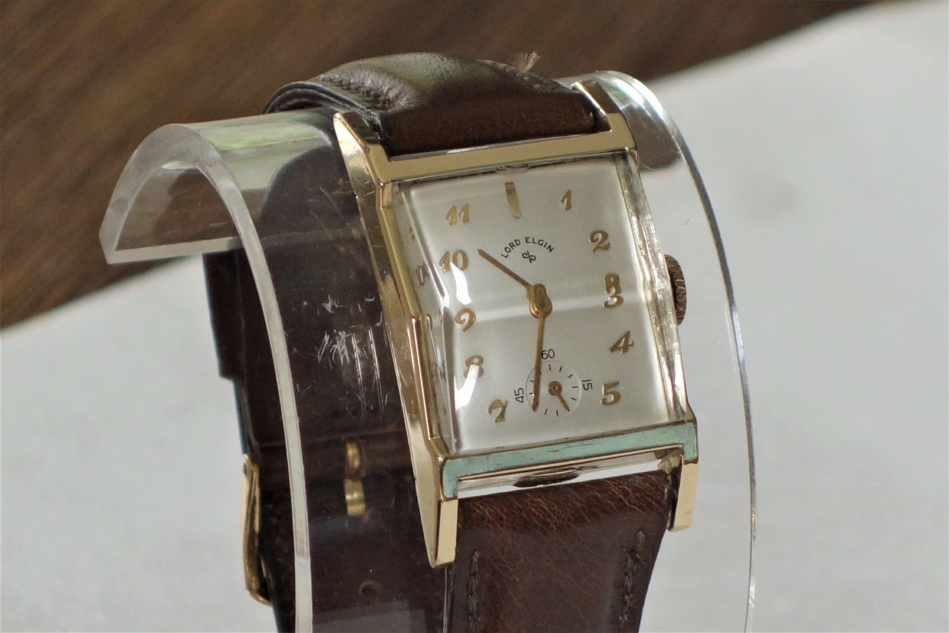 Rechteckige Armbanduhr mit braunem Armband und hellem Zifferblatt.