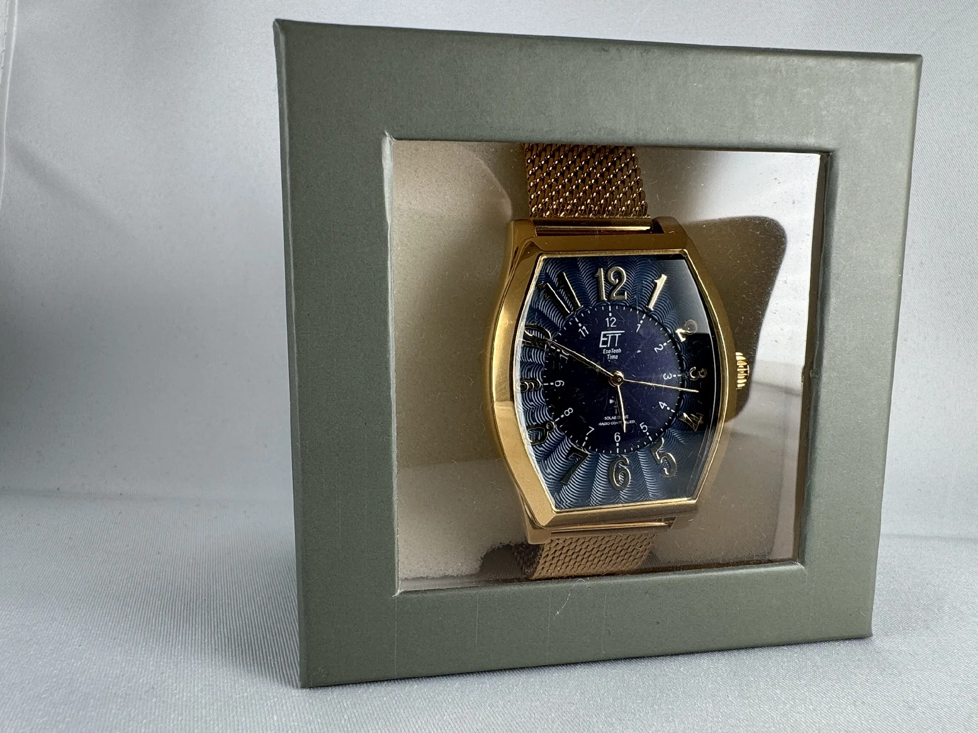 Goldfarbene Armbanduhr mit blauem Zifferblatt und Mesharmband in Geschenkbox.