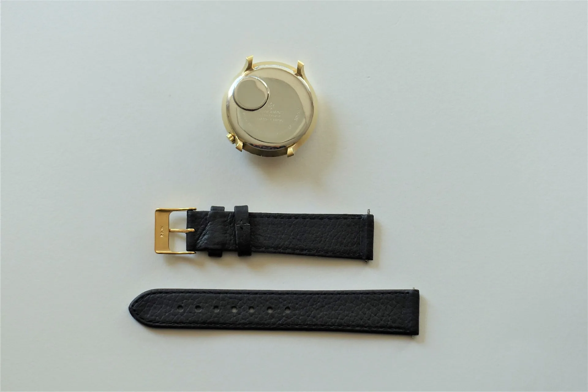 Uhrgehäuse mit Lederarmband Rundes Uhrgehäuse in heller Farbe mit schwarzem Lederarmband in zwei Teilen und goldfarbener Schließe.