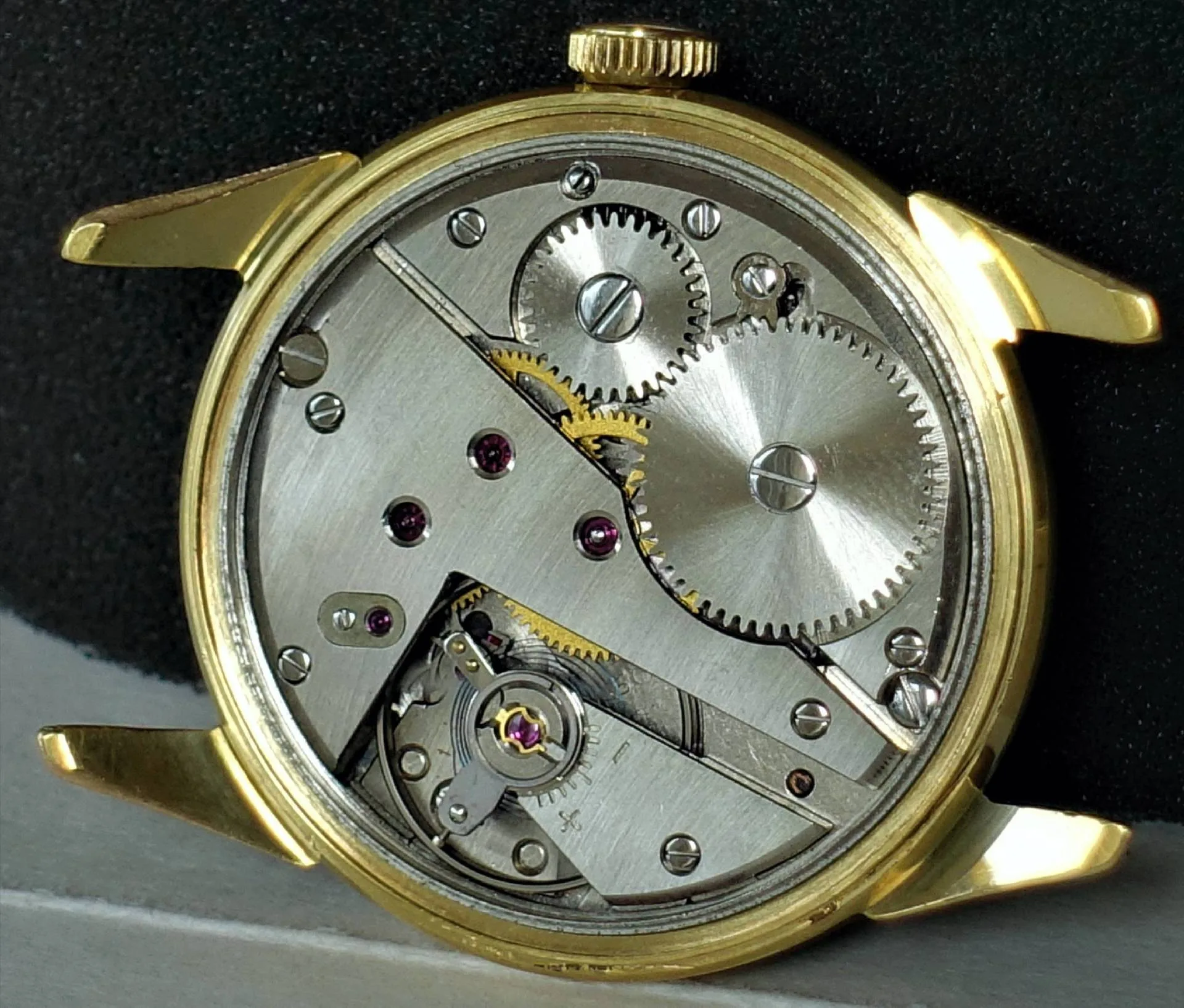 Mechanisches Uhrwerk in einem goldfarbenen Uhrengehäuse mit sichtbaren Zahnrädern und Schrauben.