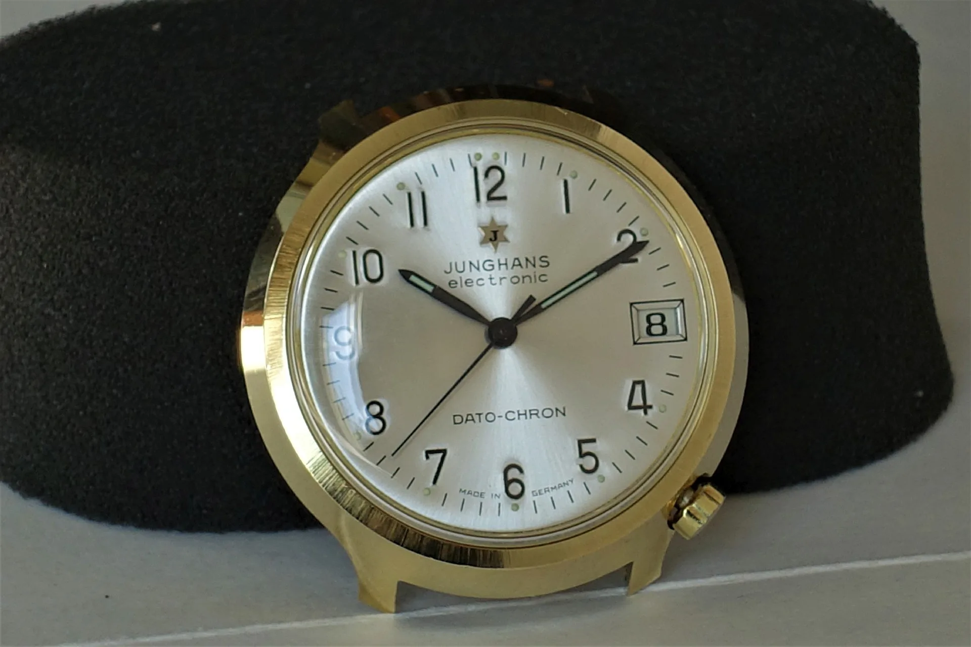 Junghans Dato-Chron Uhr Runde Armbanduhr mit hellem Zifferblatt, schwarzer Beschriftung und goldfarbenem Gehäuse.