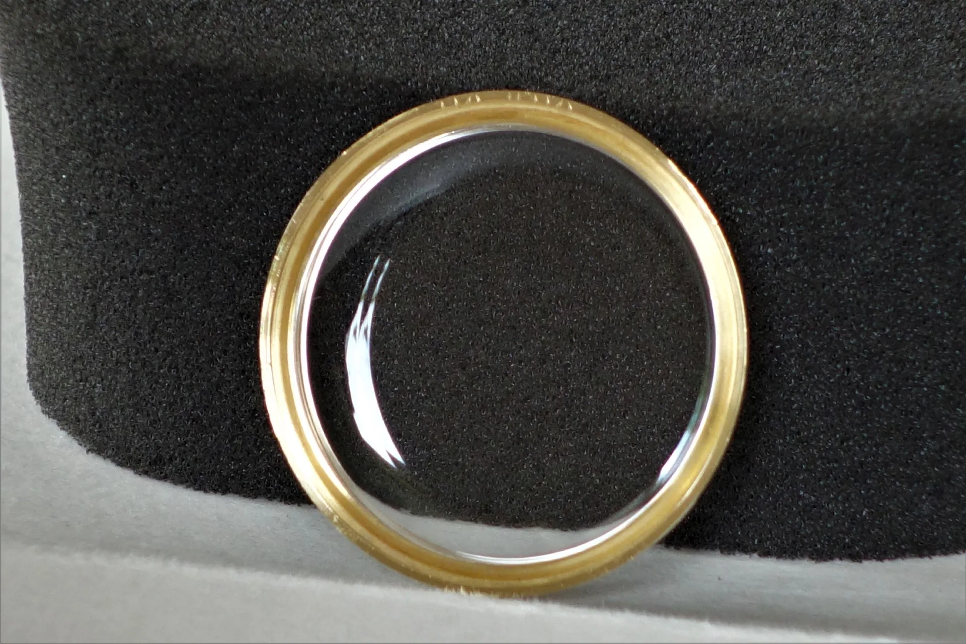 Rundes, transparentes Uhrglas mit goldfarbenem Rahmen.