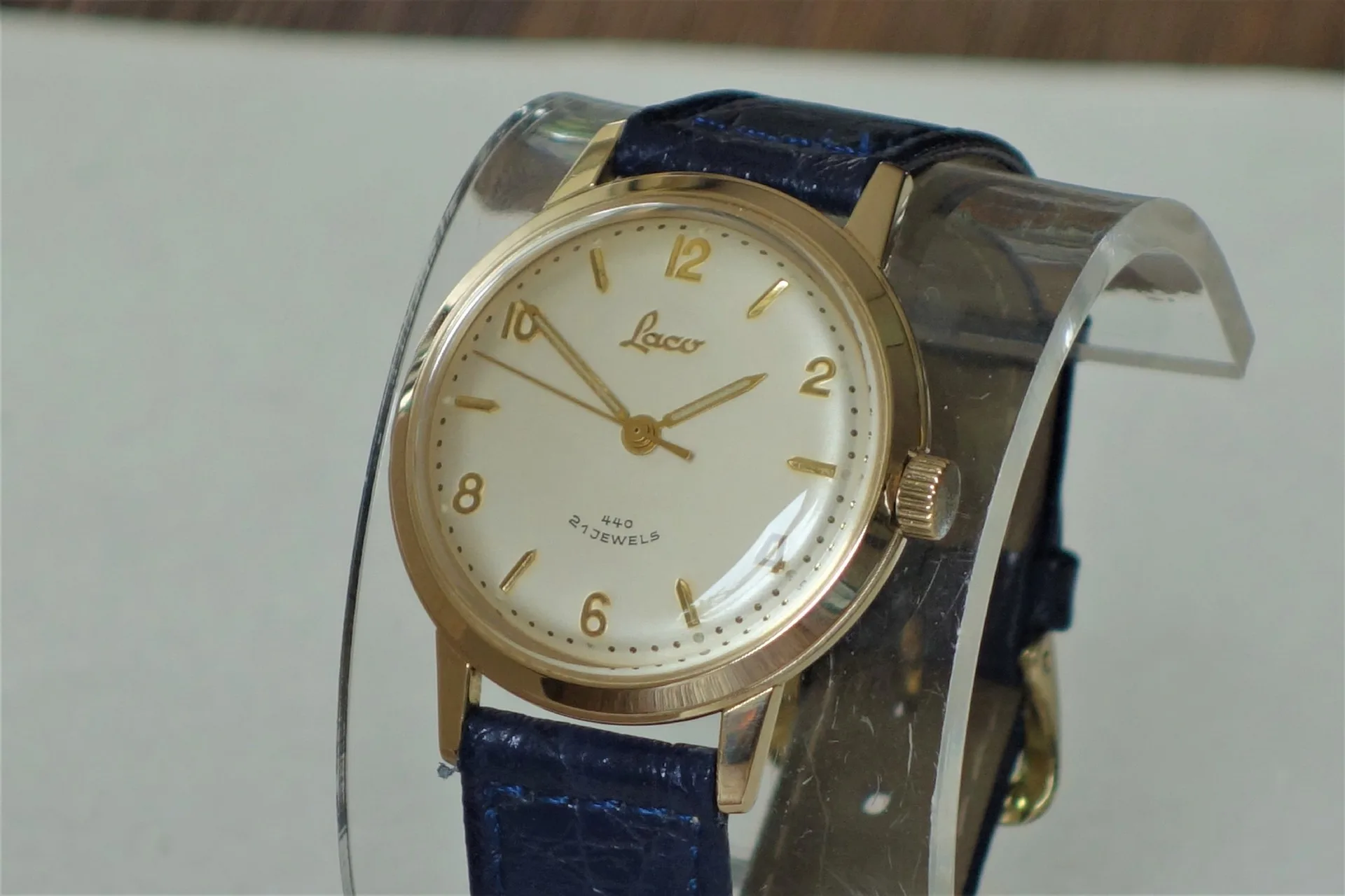 Goldfarbene Armbanduhr mit hellem Zifferblatt und blauem Armband.