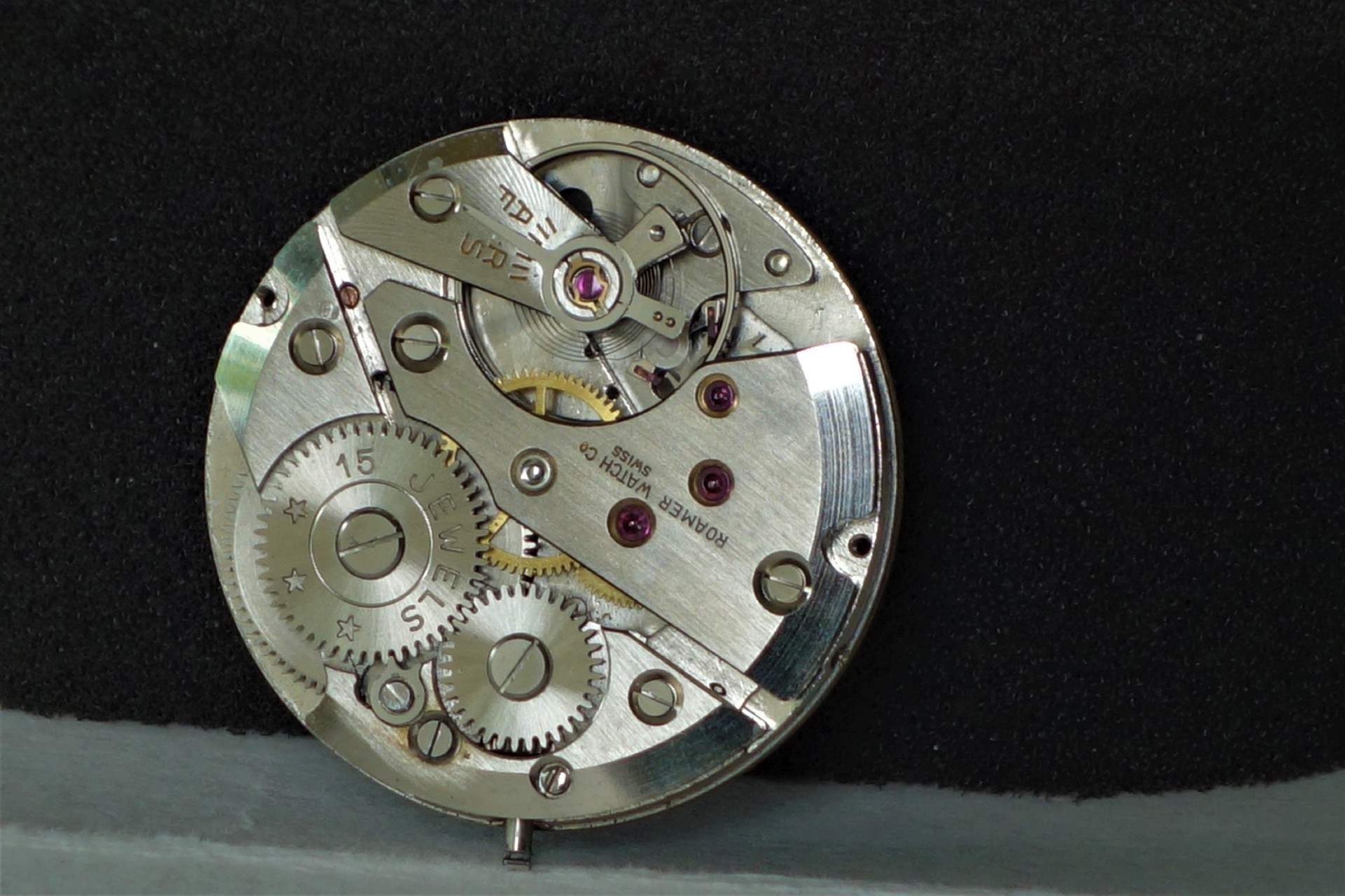 Mechanisches Uhrwerk in silberner Farbe mit sichtbaren Zahnrädern und roten Lagersteinen.