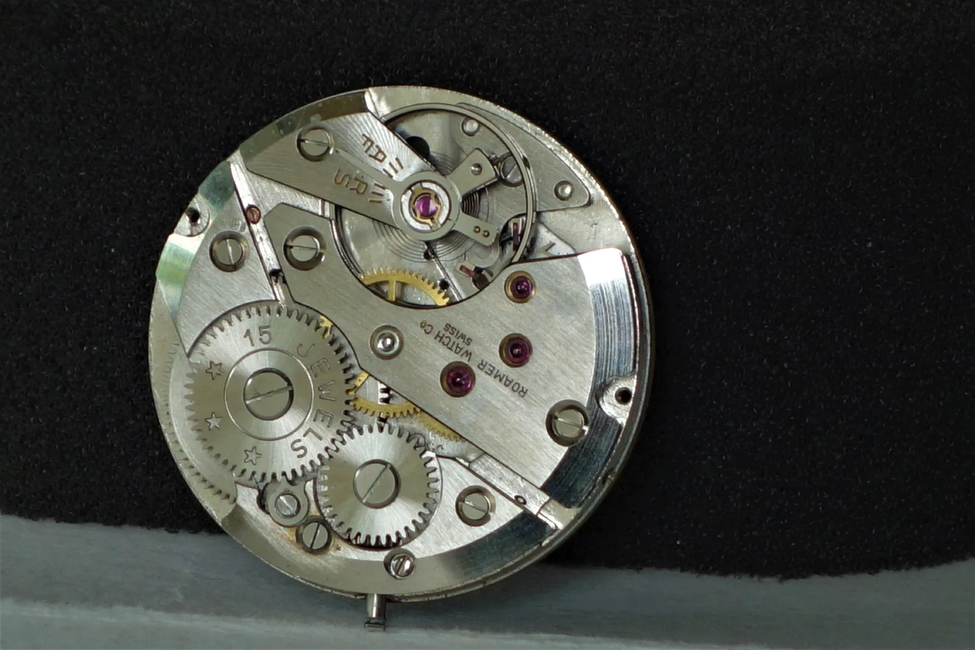 Mechanisches Uhrwerk in silberner Farbe mit sichtbaren Zahnrädern und roten Lagersteinen.