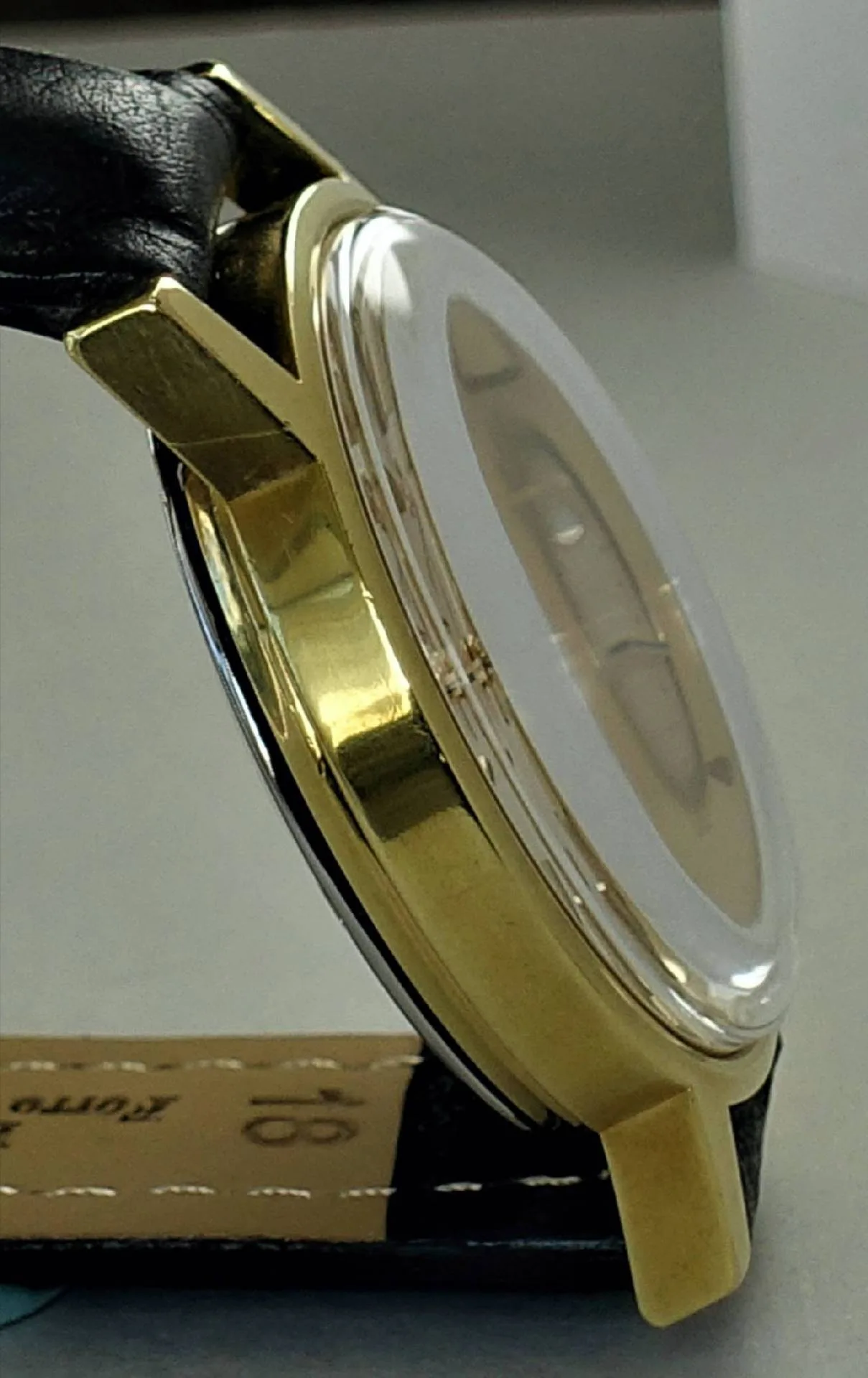 Armbanduhr goldfarben Goldfarbenes Uhrengehäuse mit schwarzem Lederarmband und gewölbtem Uhrglas.
