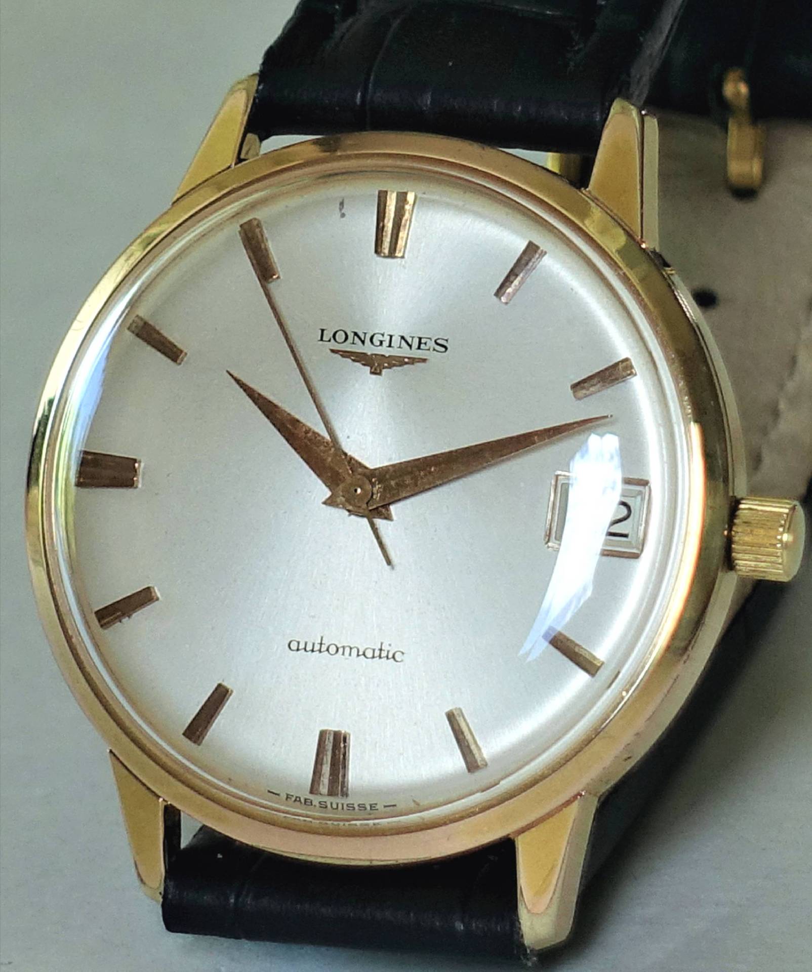 Goldfarbene Armbanduhr mit hellem Zifferblatt, schwarzem Armband und Datumsanzeige.