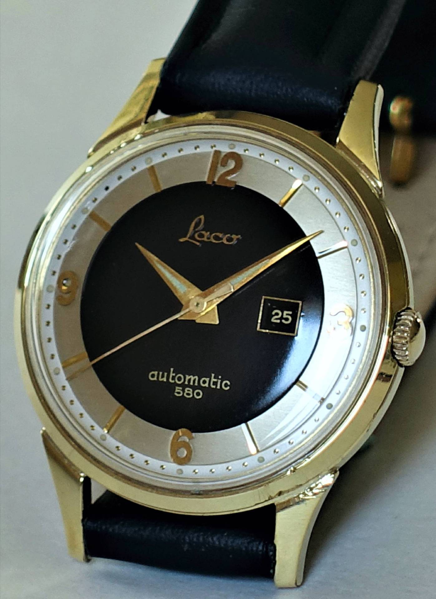 Goldfarbene Armbanduhr mit schwarzem Zifferblatt, Datumsanzeige und schwarzem Armband.