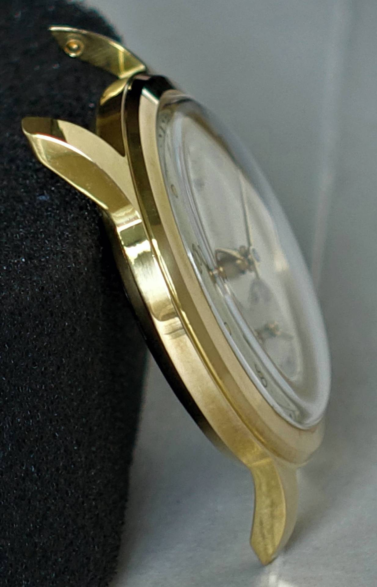 Goldfarbenes Uhrgehäuse mit montiertem Glas und Zifferblatt.