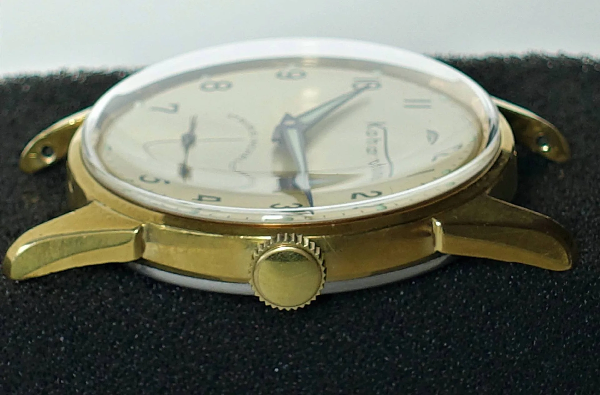 Goldfarbene Armbanduhr mit hellem Zifferblatt und schwarzen Zahlen.
