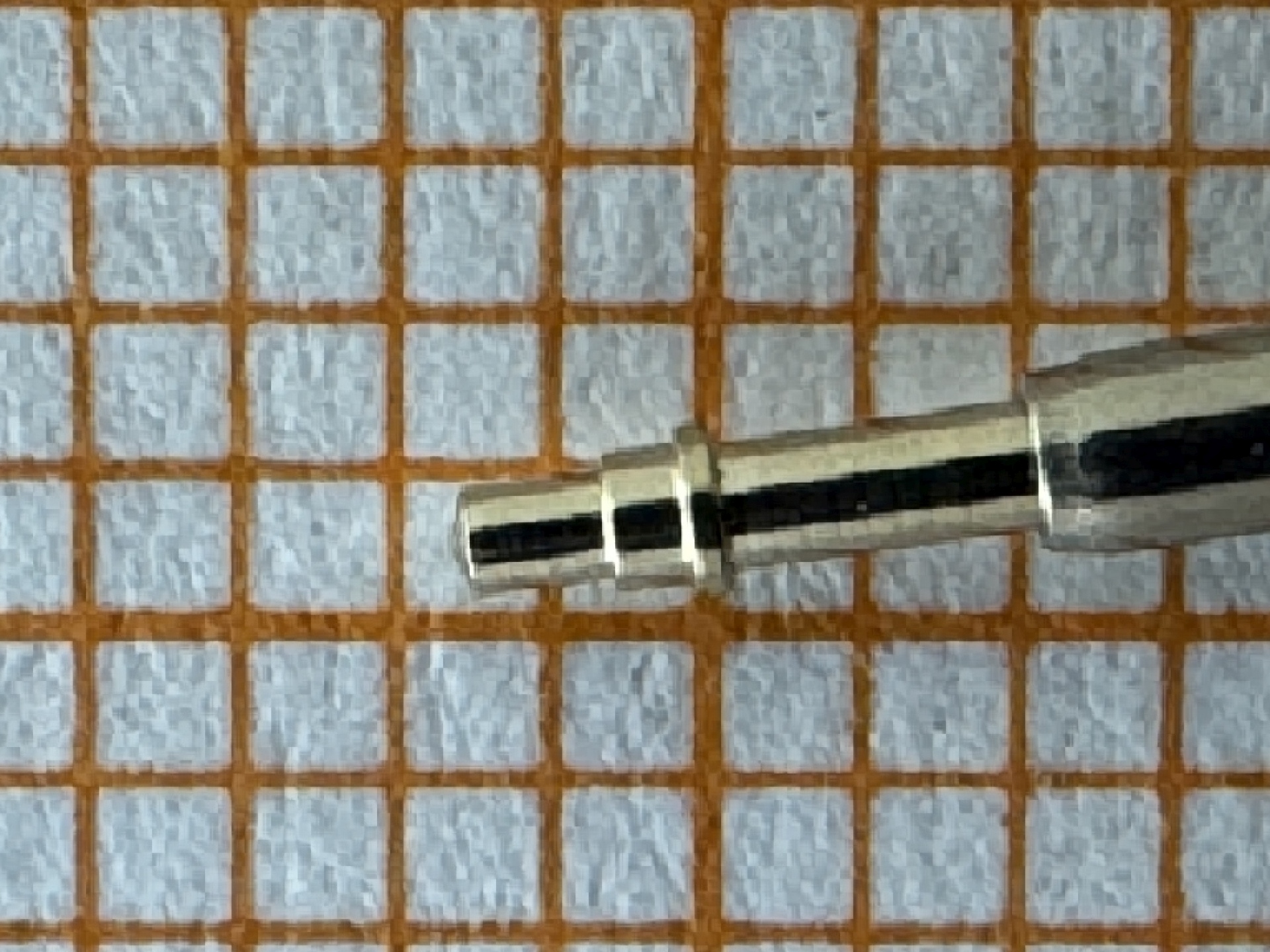 Metallstift zum Befestigen von Uhrenarmbändern auf einem karierten Untergrund.