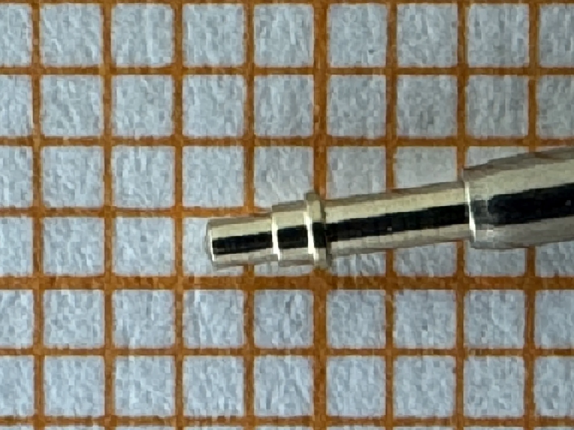 Metallstift zum Befestigen von Uhrenarmbändern auf einem karierten Untergrund.