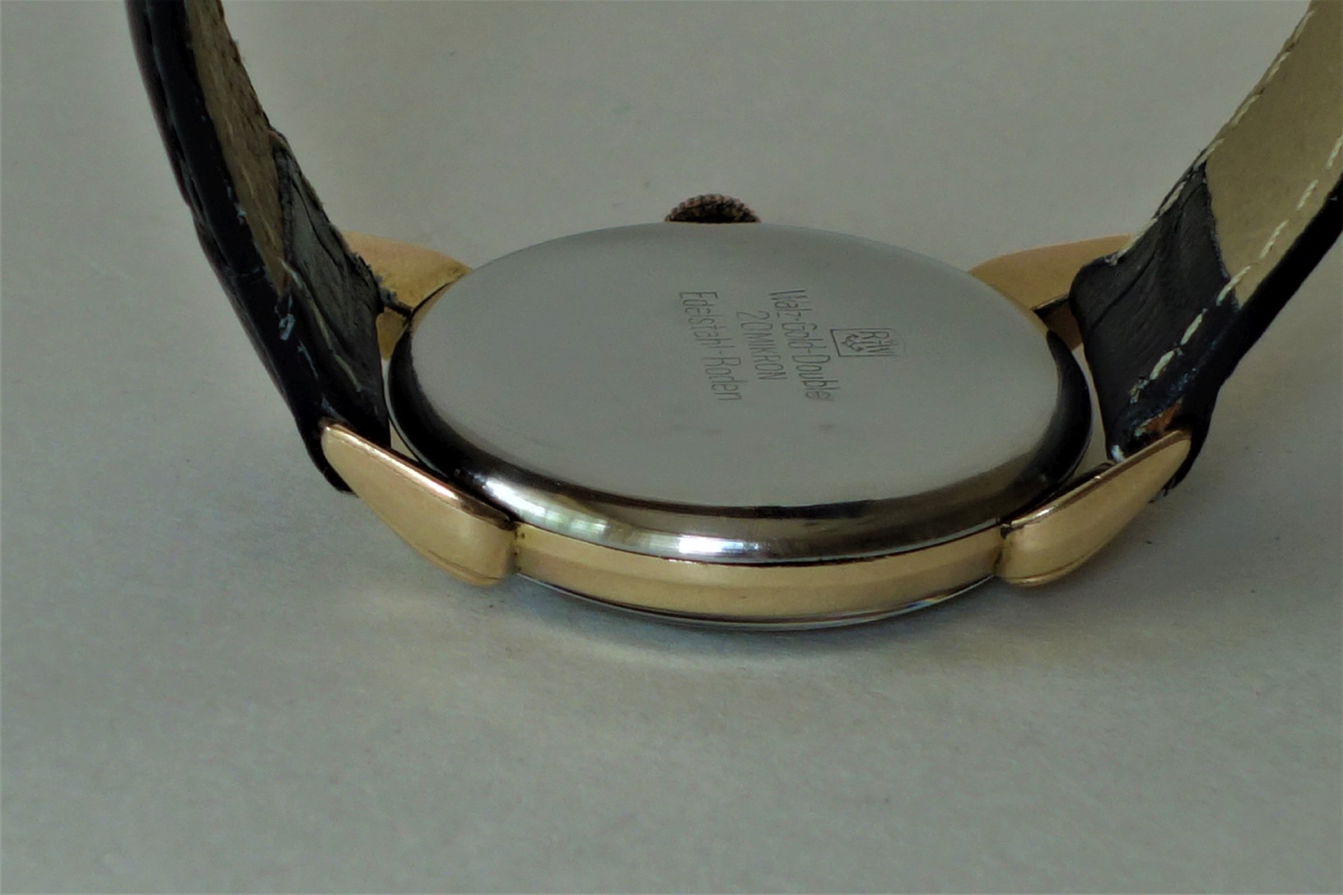 Silberfarbener runder Uhrenboden an einer Armbanduhr mit schwarzem Armband.