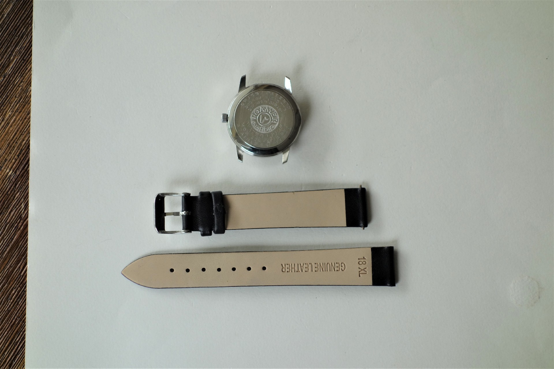 Silberfarbenes Uhrgehäuse und zweiteiliges schwarzes Lederarmband für Armbanduhren.