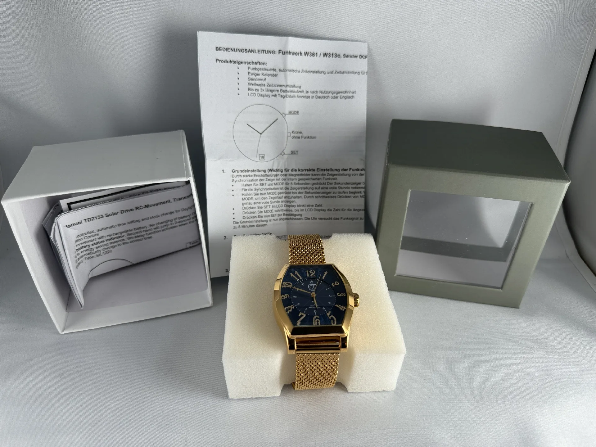 Goldfarbene Funkarmbanduhr mit blauem Zifferblatt und Mesharmband, inklusive Verpackung und Bedienungsanleitung.