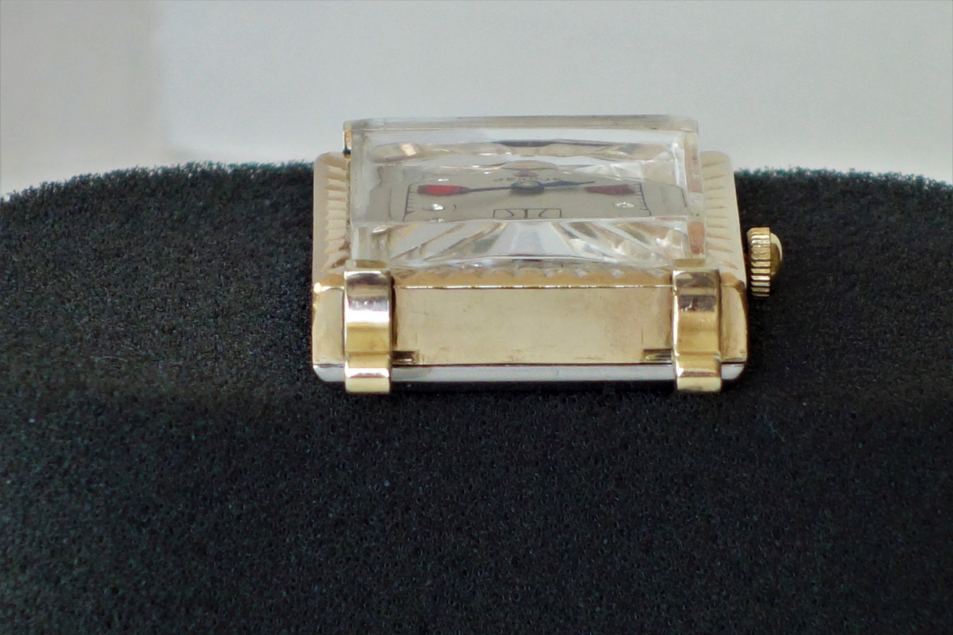 Rechteckige Armbanduhr mit goldfarbenem Metallgehäuse und facettiertem Uhrglas.