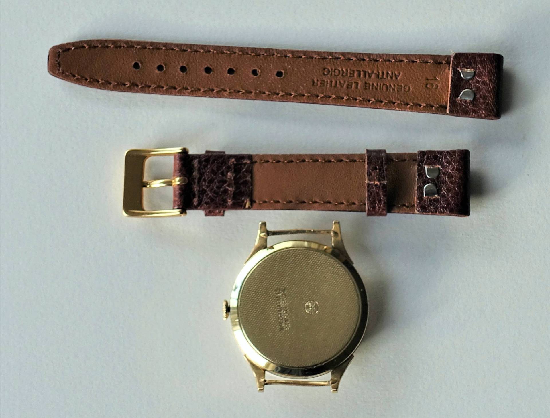 Goldfarbenes Uhrgehäuse mit braunem Lederarmband und goldfarbener Schließe.