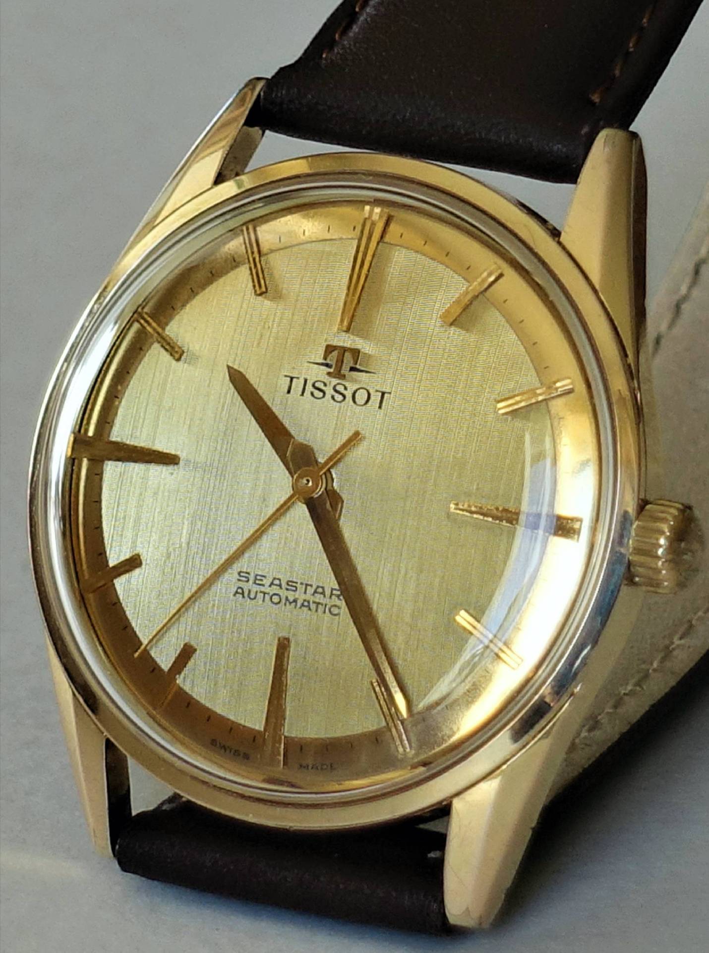 Goldfarbene Armbanduhr mit hellem Zifferblatt und braunem Armband, Modell Tissot Seastar Automatic.