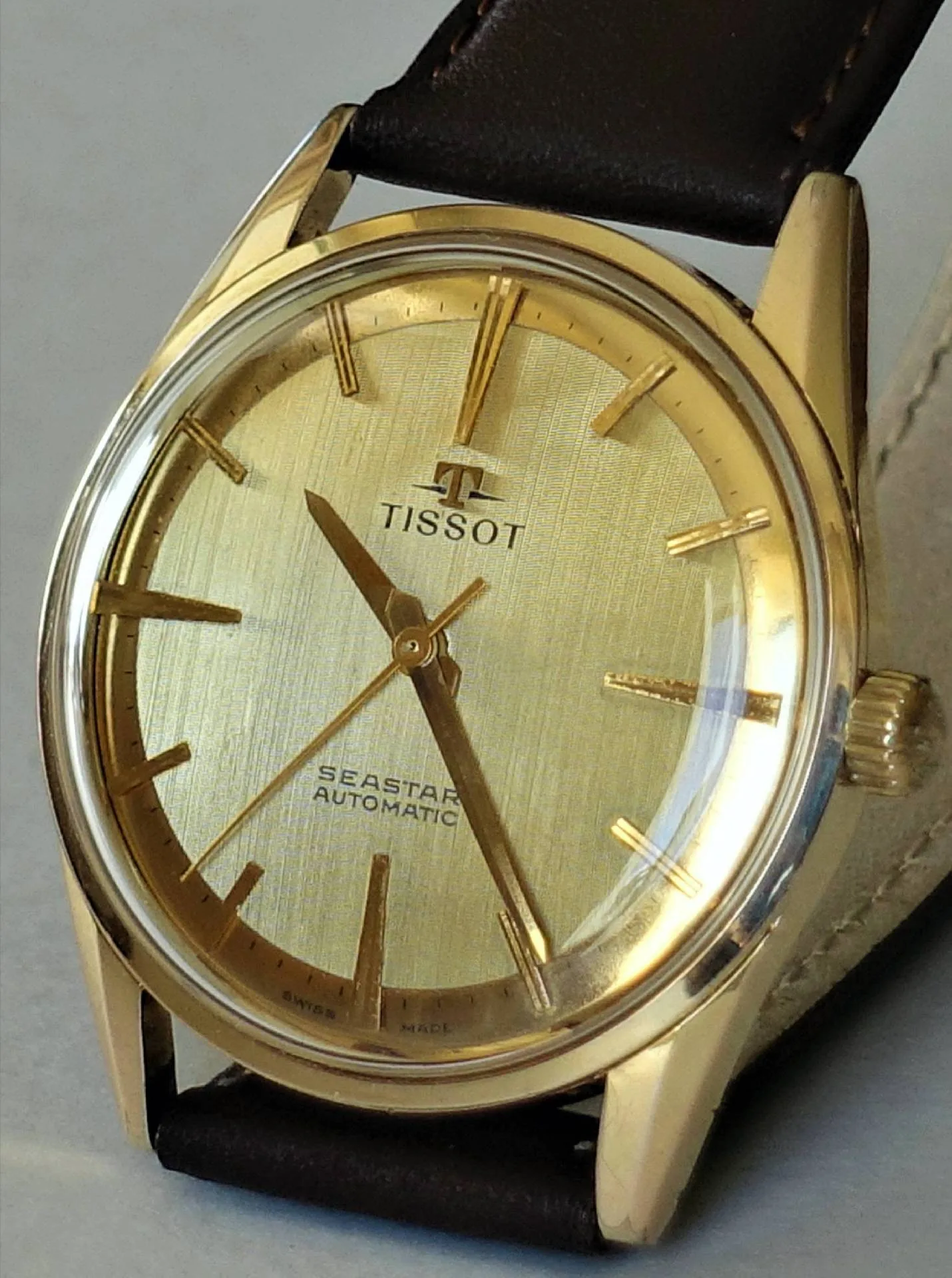 Goldfarbene Armbanduhr mit hellem Zifferblatt und braunem Armband, Modell Tissot Seastar Automatic.