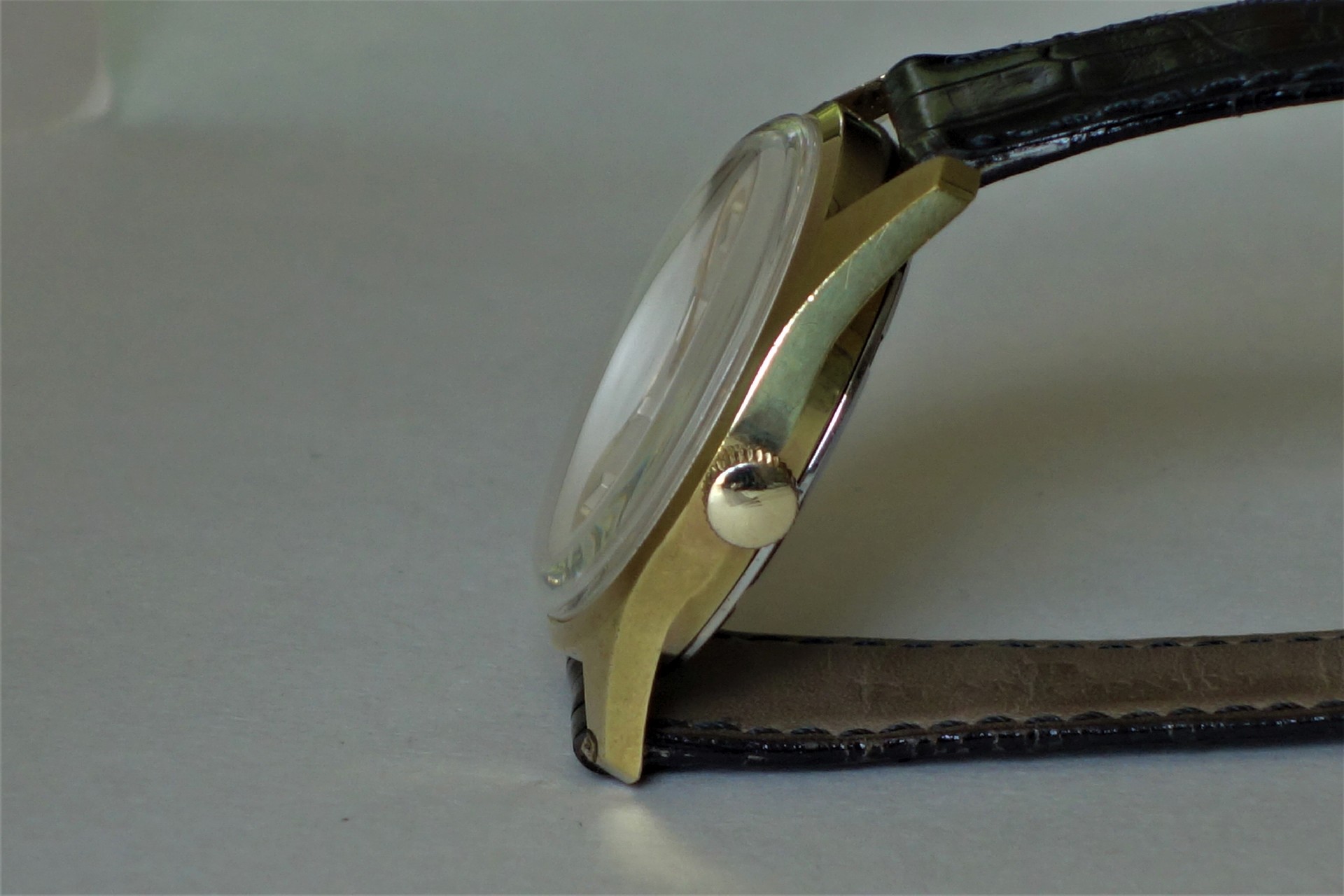 Flache Armbanduhr mit goldfarbenem Gehäuse und schwarzem Lederarmband in Seitenansicht.