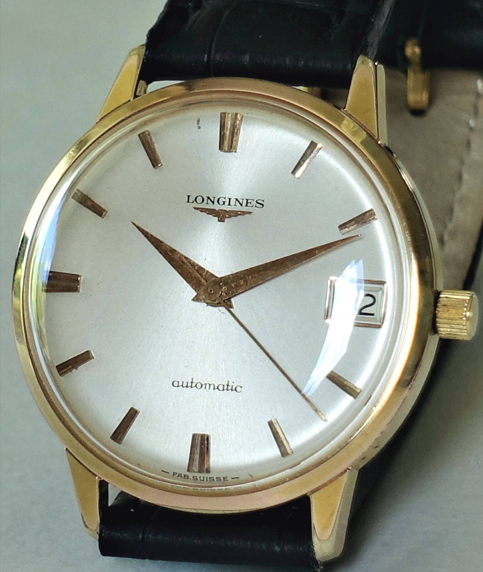 Goldfarbene Armbanduhr mit silberfarbenem Zifferblatt, Datumsanzeige und schwarzem Armband.