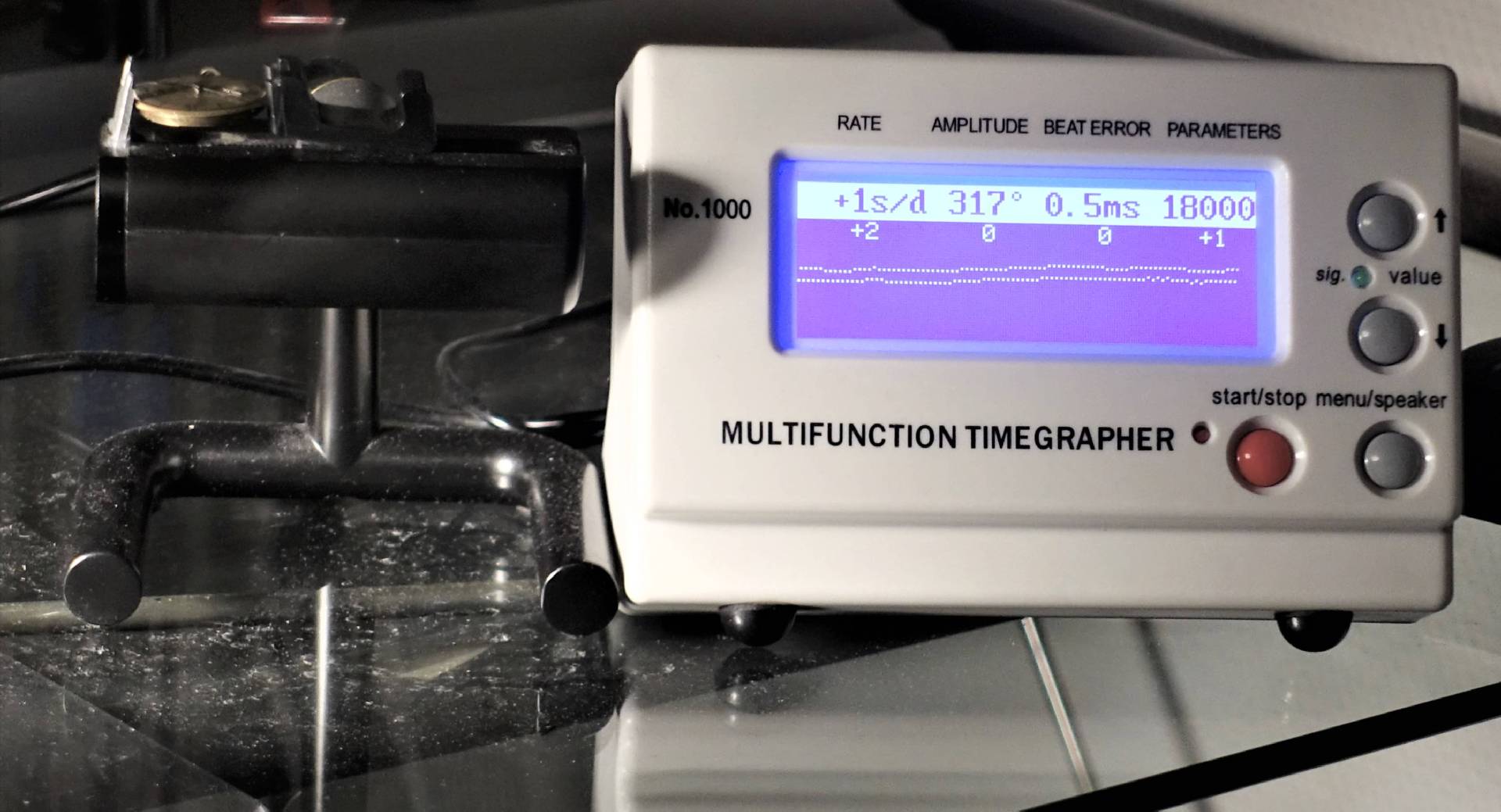 Ein weißes elektronisches Zeitwaagenmessgerät mit blauem Display steht auf einem Tisch und misst die Gangwerte einer Uhr.