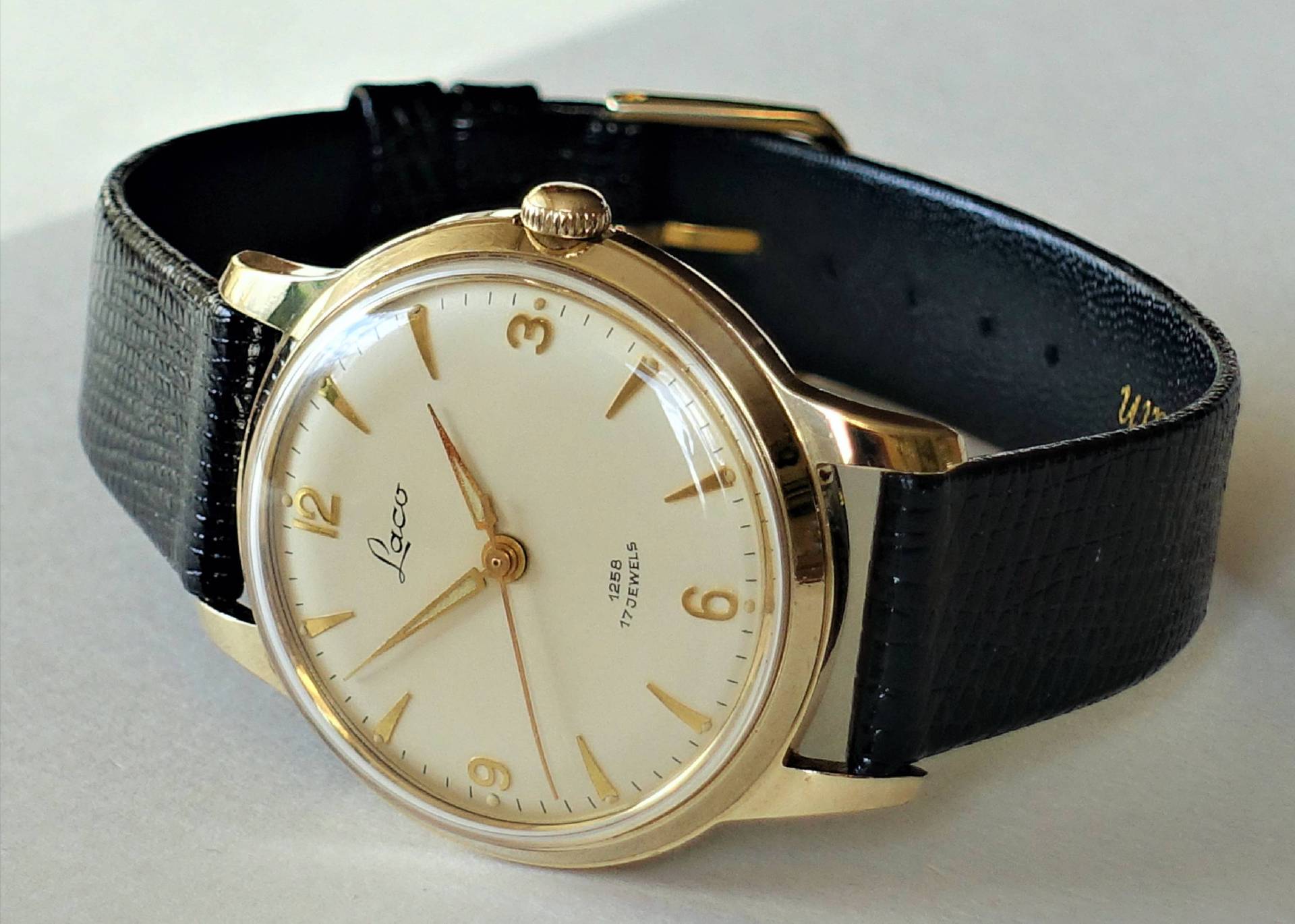 Goldfarbene Armbanduhr mit hellem Zifferblatt und schwarzem Armband.