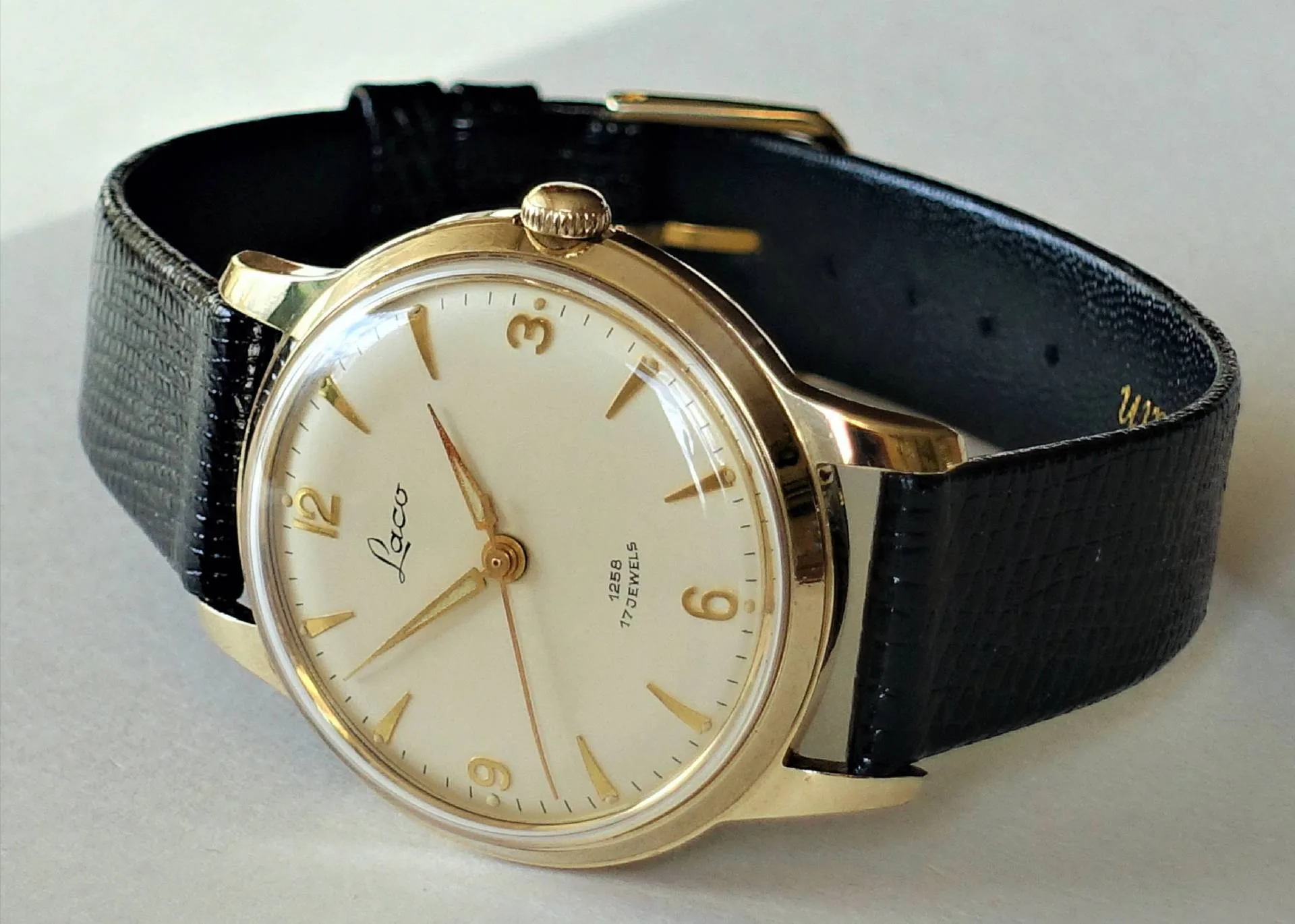 Goldfarbene Armbanduhr mit hellem Zifferblatt und schwarzem Armband.
