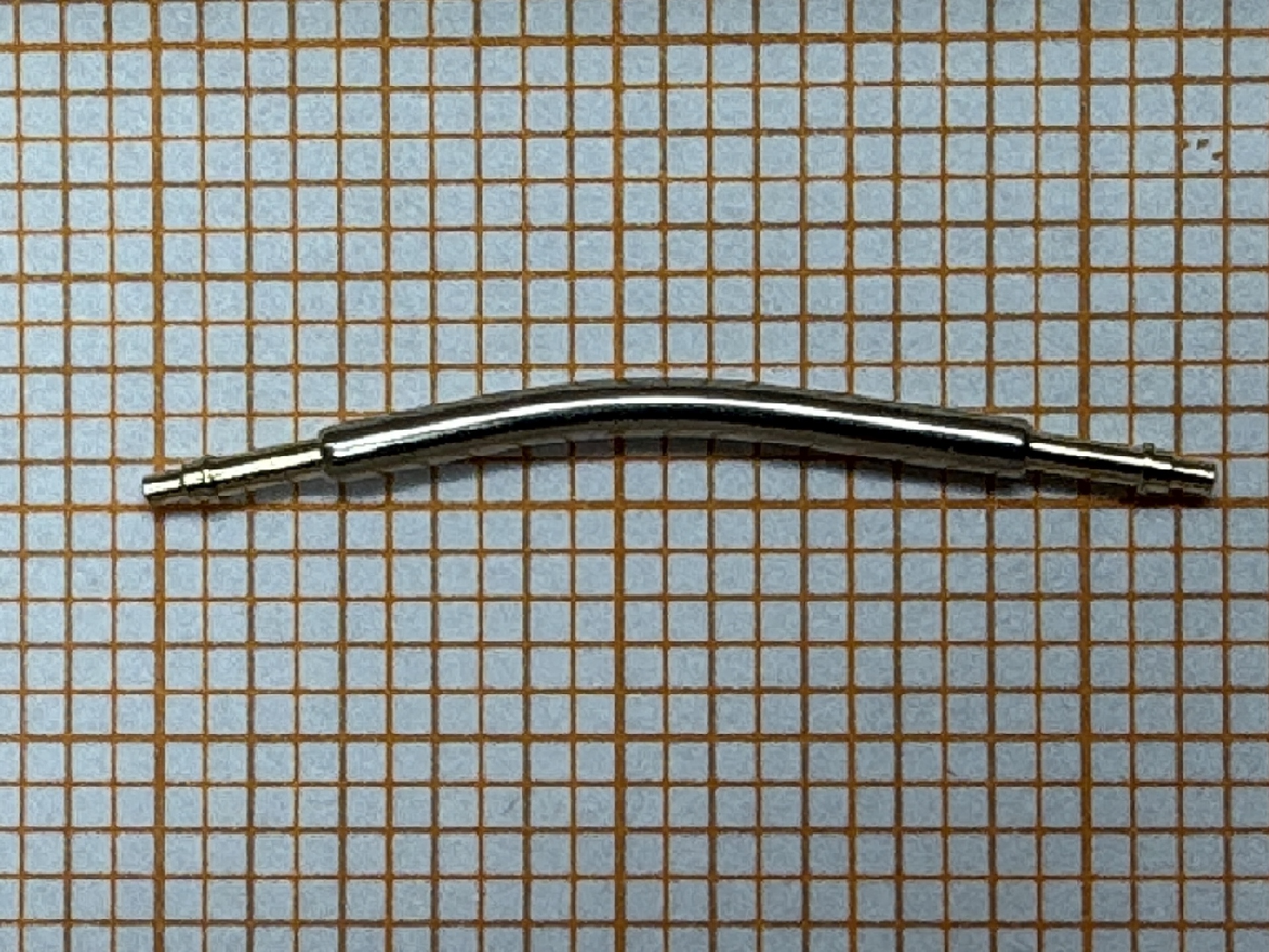 Gebogener Metall-Federsteg für Uhrenarmbänder auf kariertem Hintergrund.