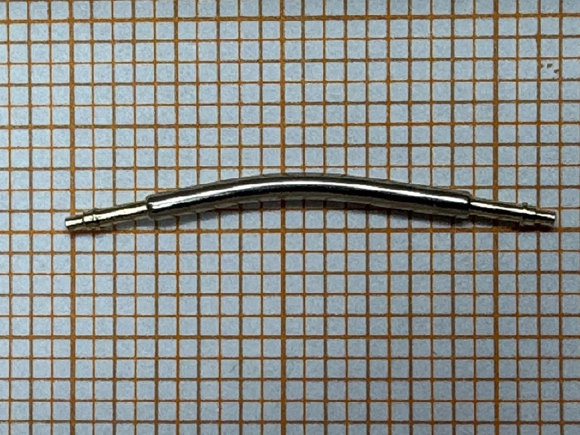 Gebogenes Federsteg Metall Gebogener Metall-Federsteg für Uhrenarmbänder auf kariertem Hintergrund.