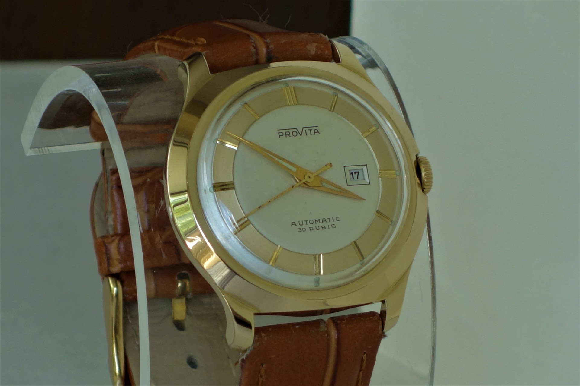 Goldfarbene Armbanduhr mit hellem Zifferblatt und braunem Armband.