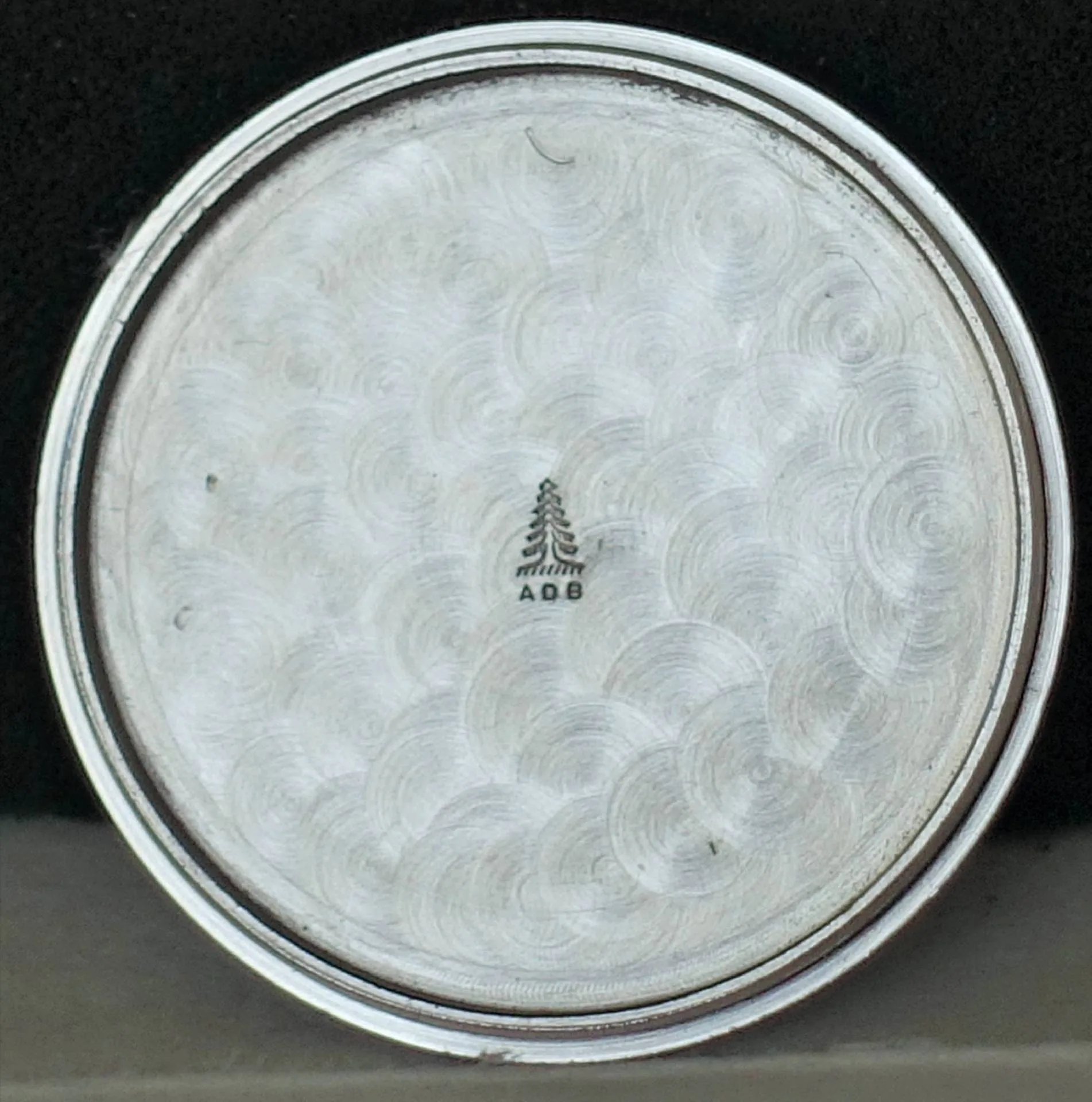 Edelstahlbecherboden mit Muster und Logo Detailaufnahme des Bodens eines Edelstahlbechers mit Wellenmuster und eingraviertem Logo.