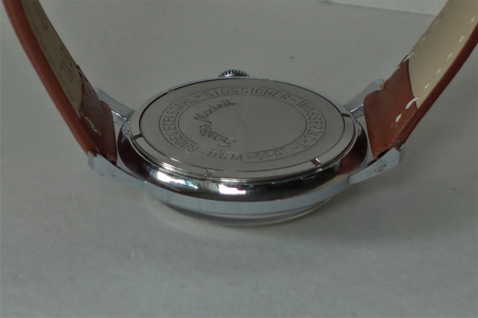 Silberfarbener Uhrenboden mit Gravur und braunem Armband.