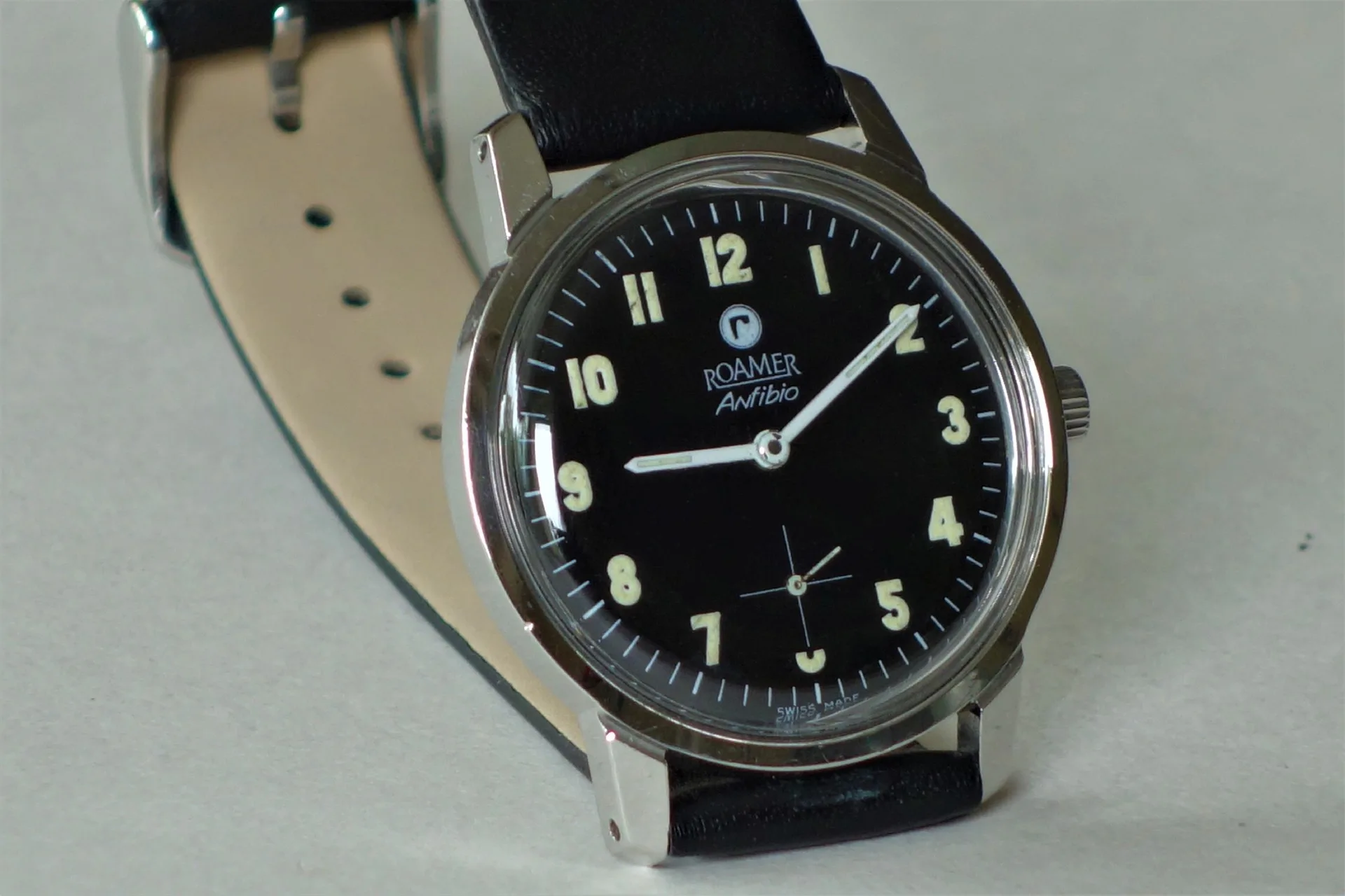 Schwarze Armbanduhr mit hellem Zifferblatt und Lederarmband.