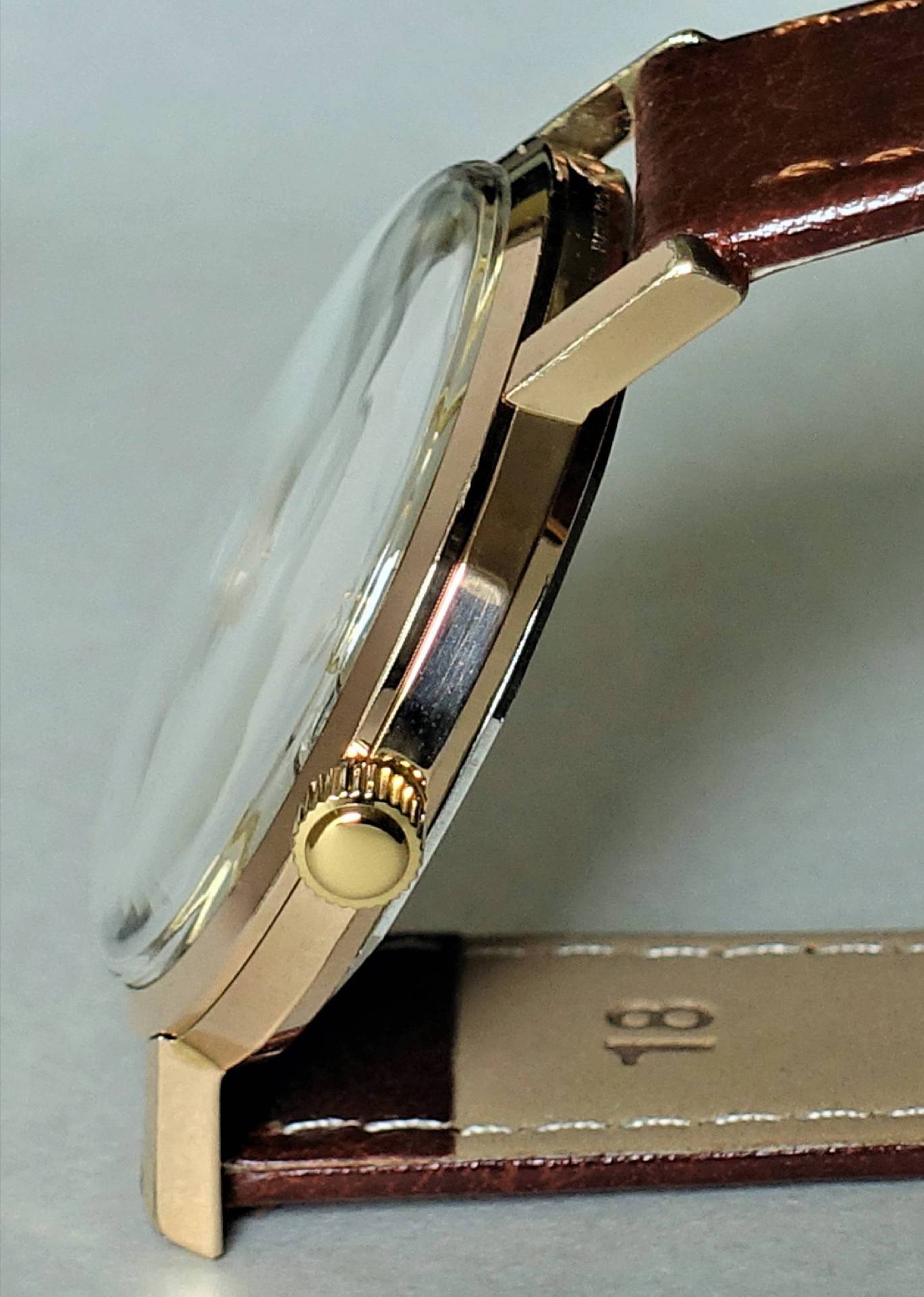 Flache Armbanduhr mit goldfarbenem Gehäuse und braunem Lederarmband.