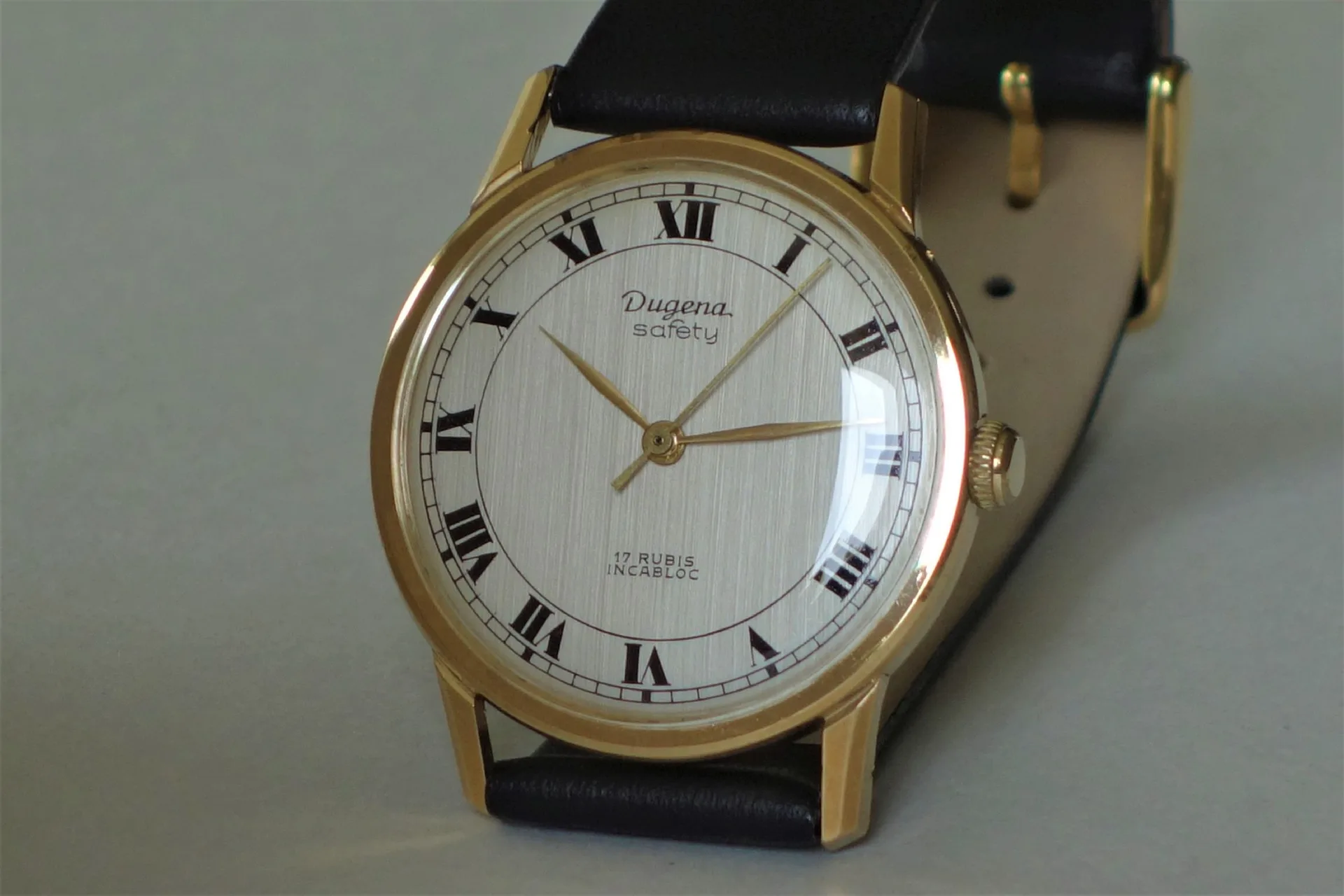 Analoge Armbanduhr mit goldfarbenem Gehäuse, weißem Zifferblatt und schwarzem Lederarmband.